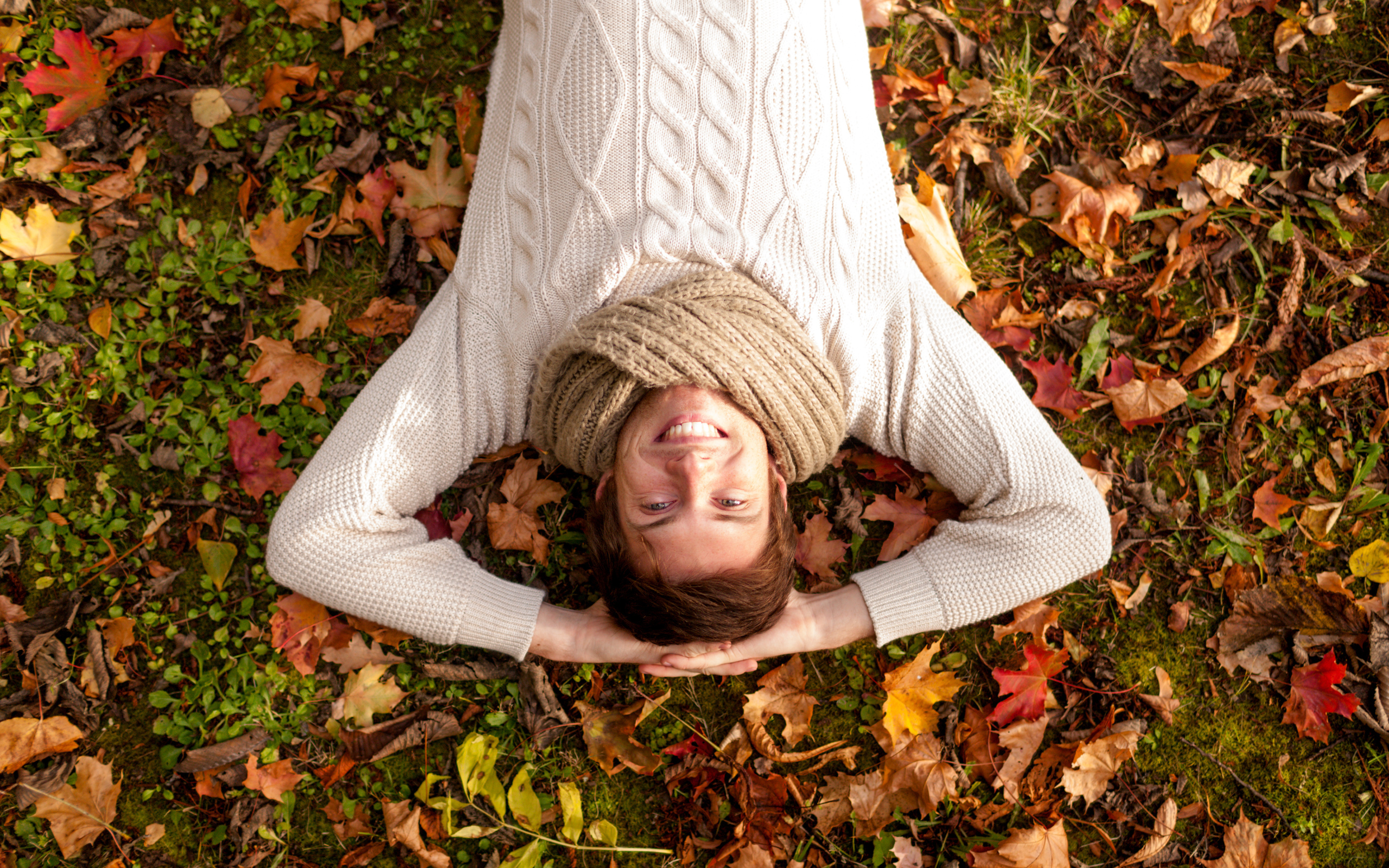 Улыбающийся мужчина в свитере лежит на опавших листьях 