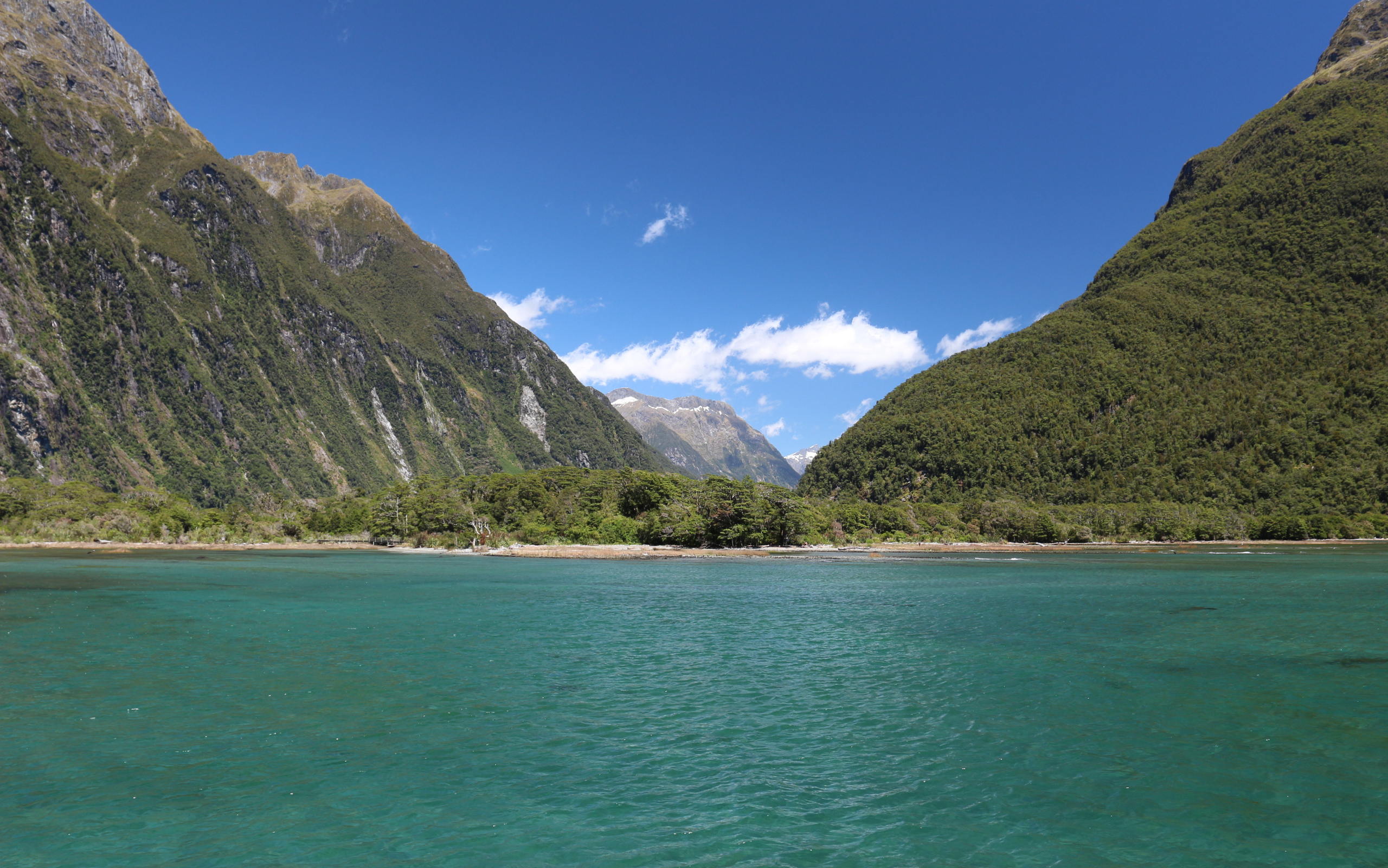 Blue water in the lake on the background of green-covered mountains under a blue sky