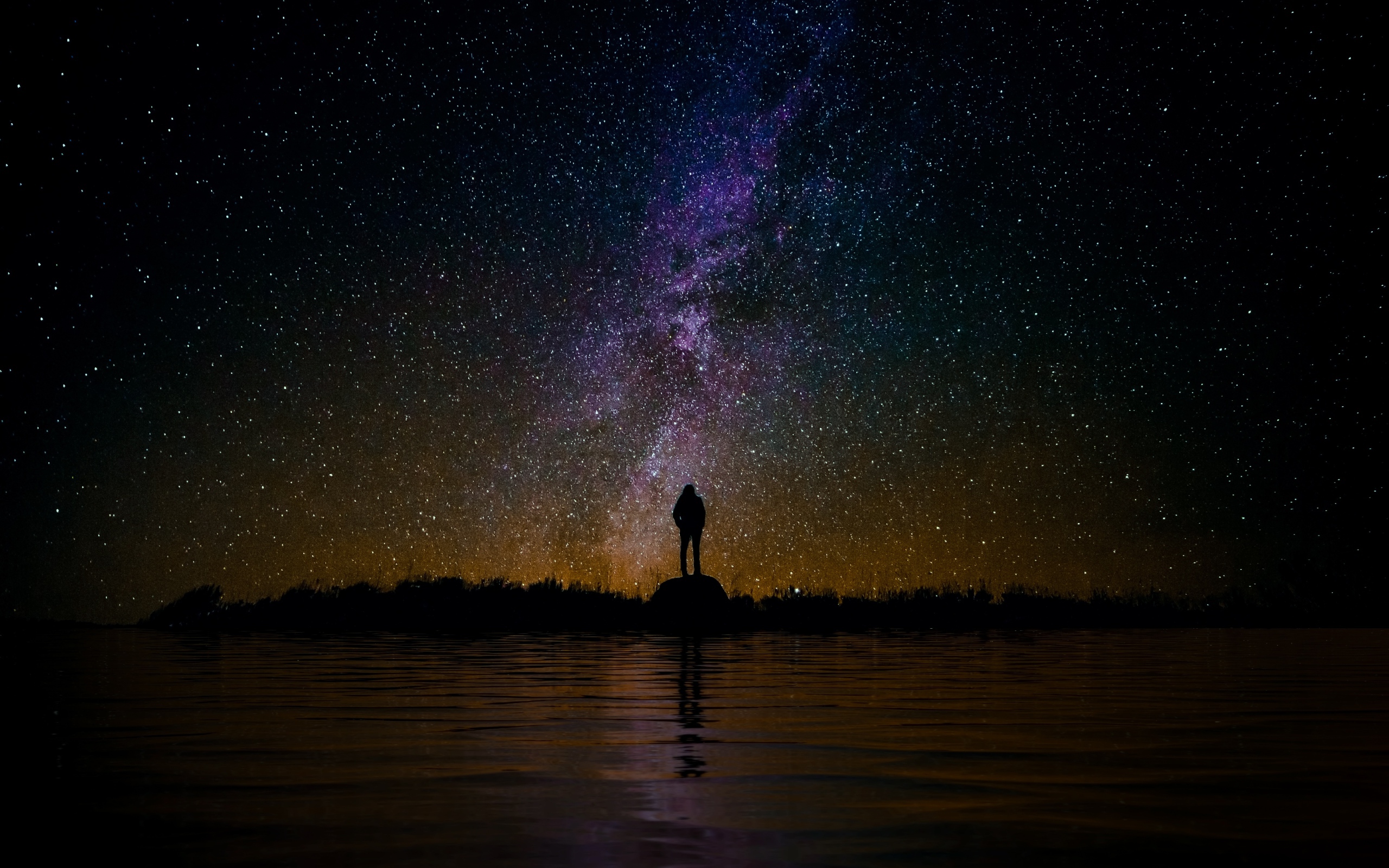 Силуэт человека стоит на камне у воды под звездным небом