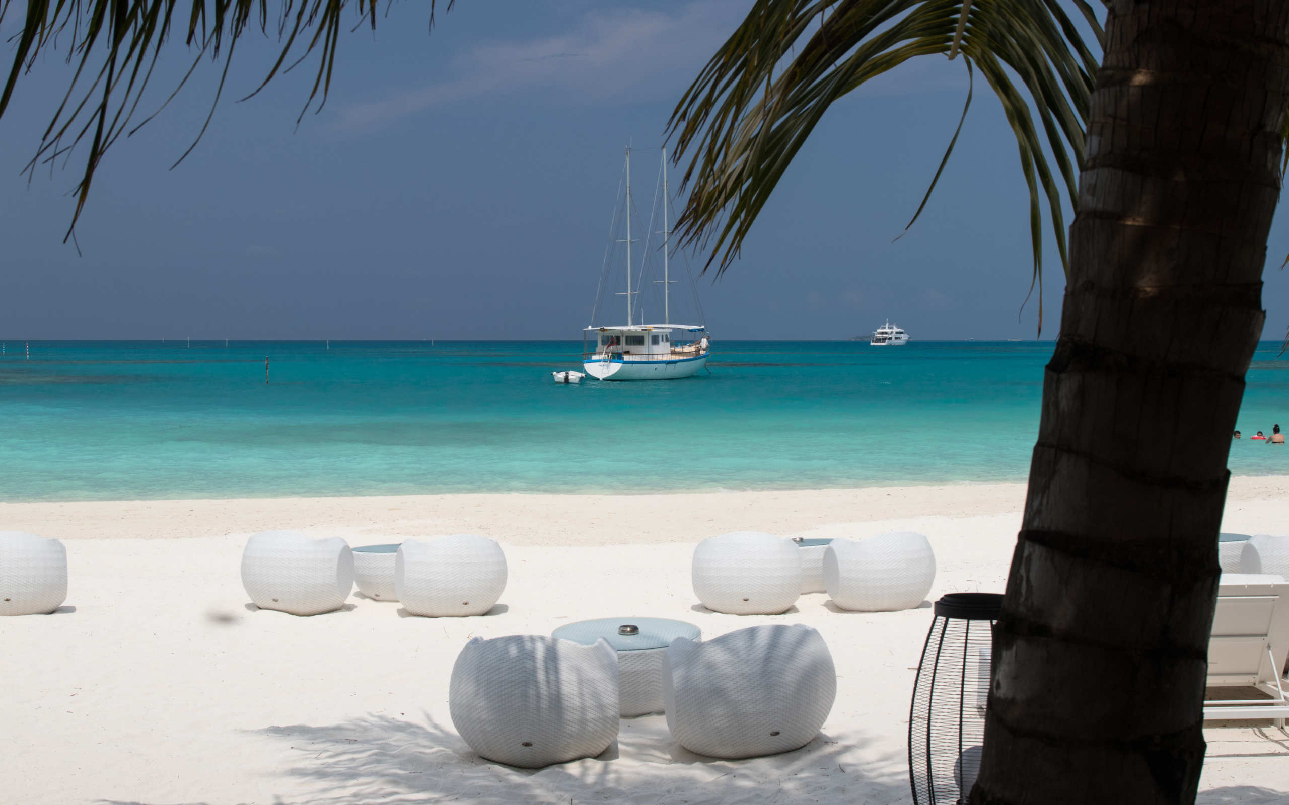 Белые кресла и столики на белом песке на пляже у голубой воды