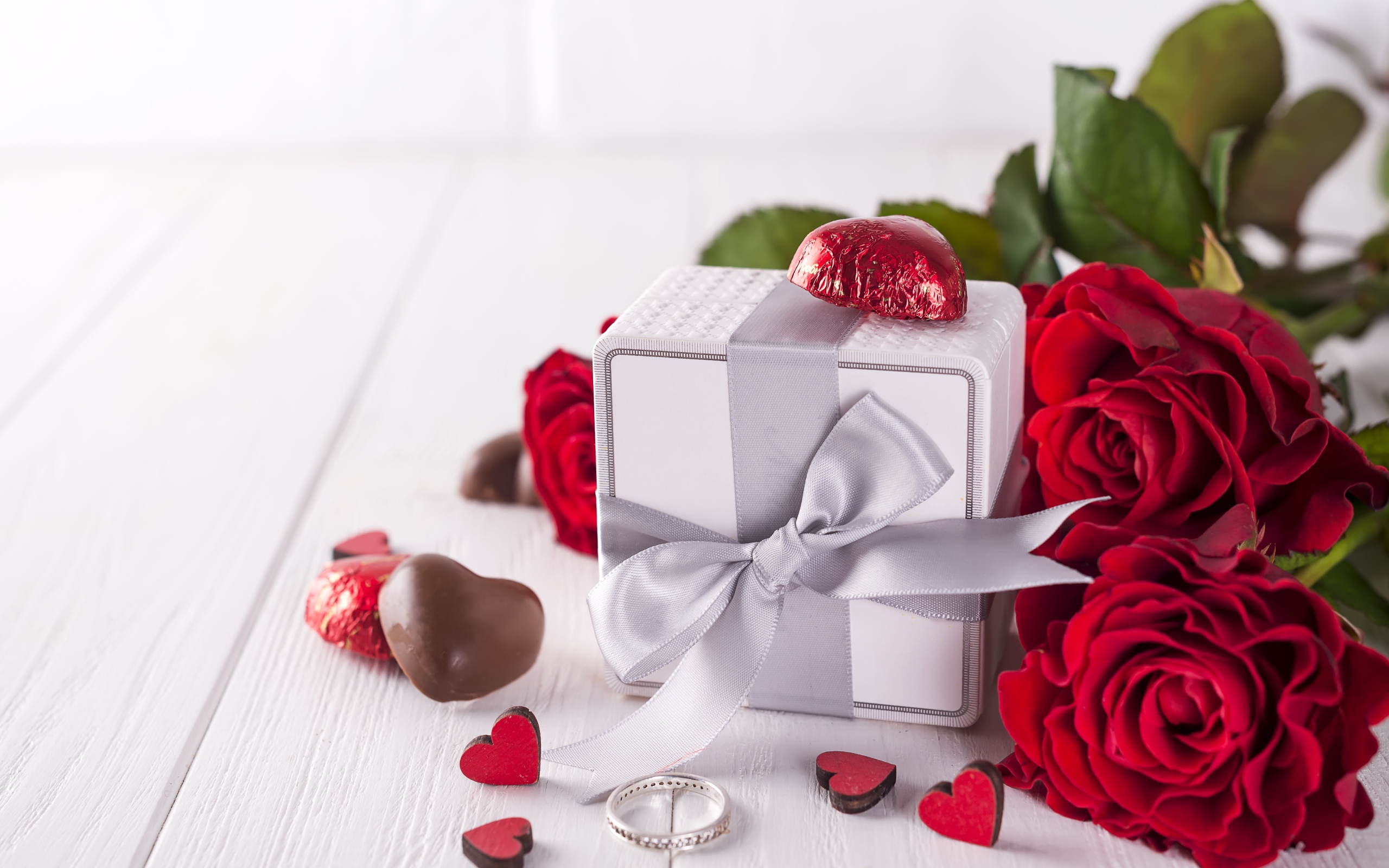 Подарок на столе с конфетами и букетом красных роз 