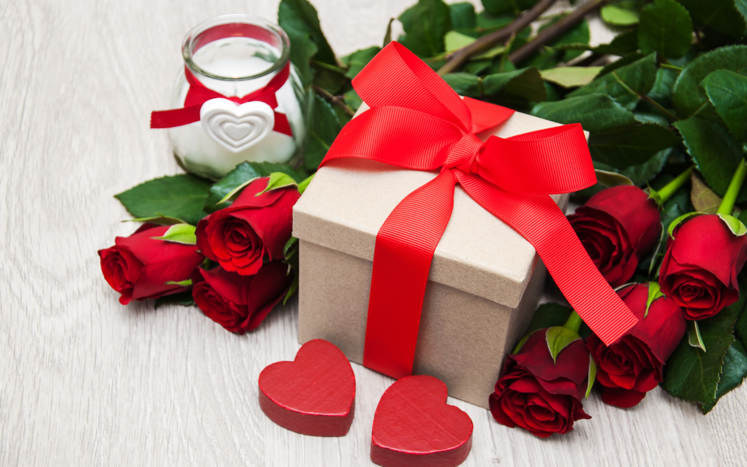 Красивый букет красных роз на столе со свечой и подарком