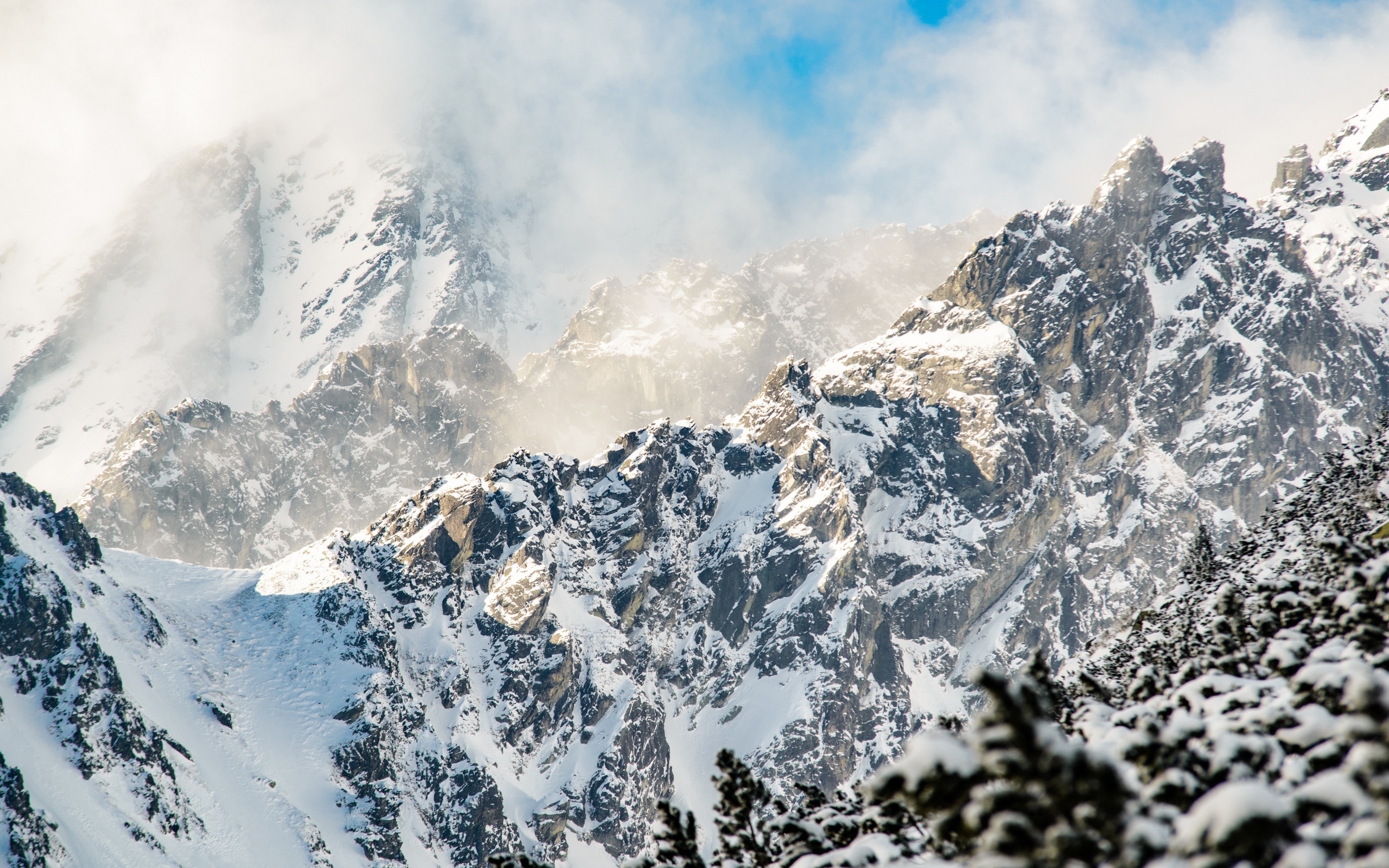 Заснеженные вершины гор под белыми облаками в голубом небе