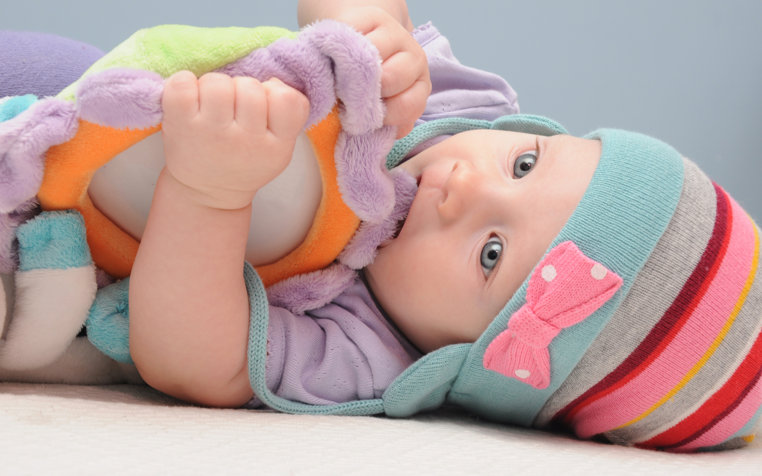 Младенец в шапке грызет мягкую игрушку