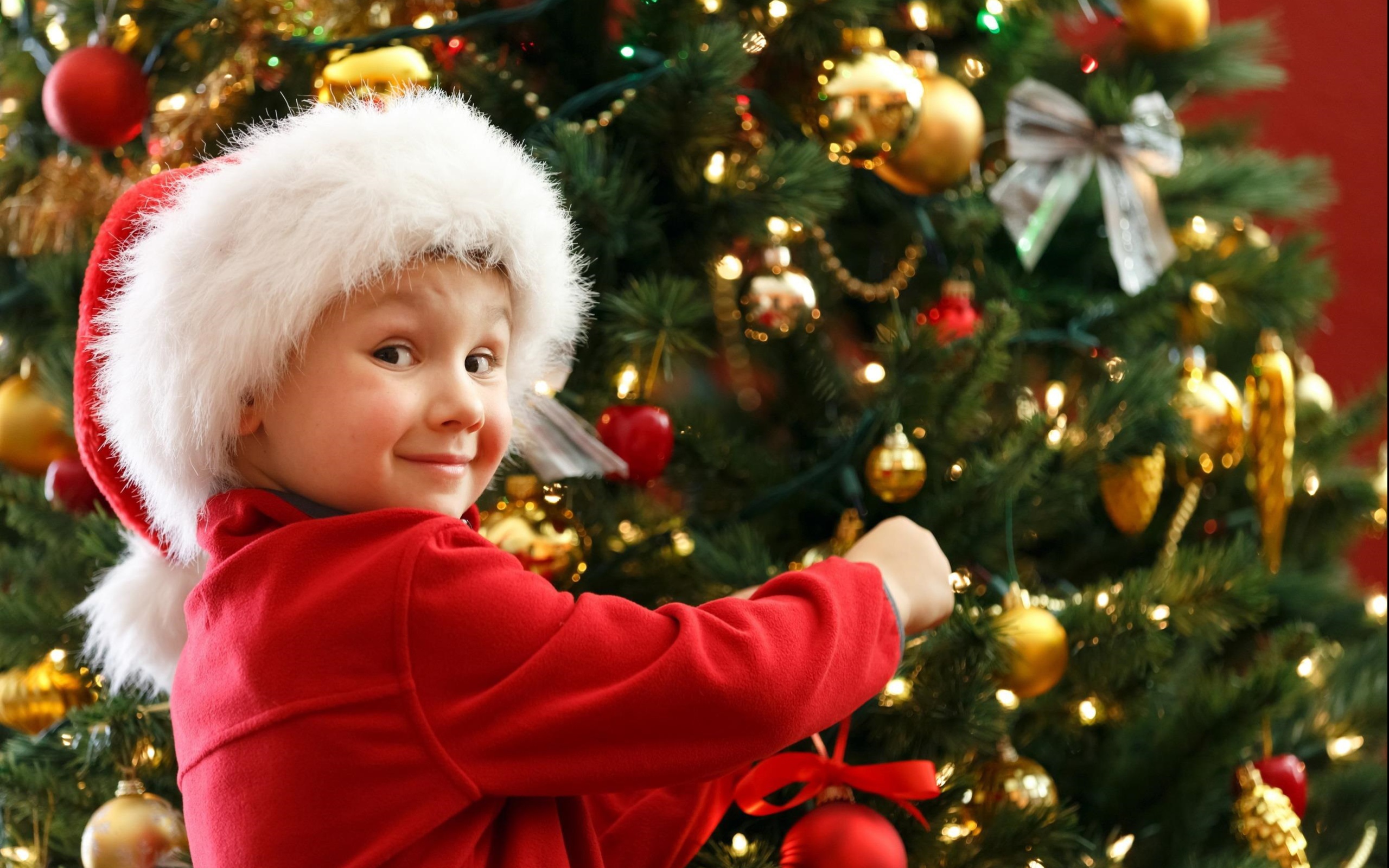Мальчик в шапке Санта Клауса наряжает елку