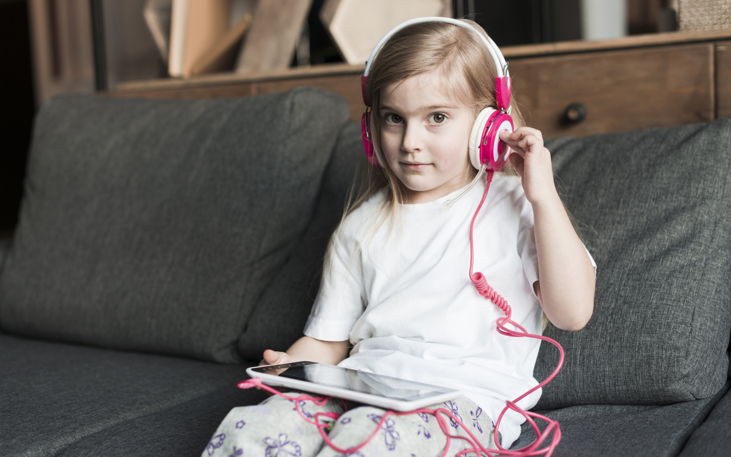 Девочка сидит на диване в наушниках  и с планшетом