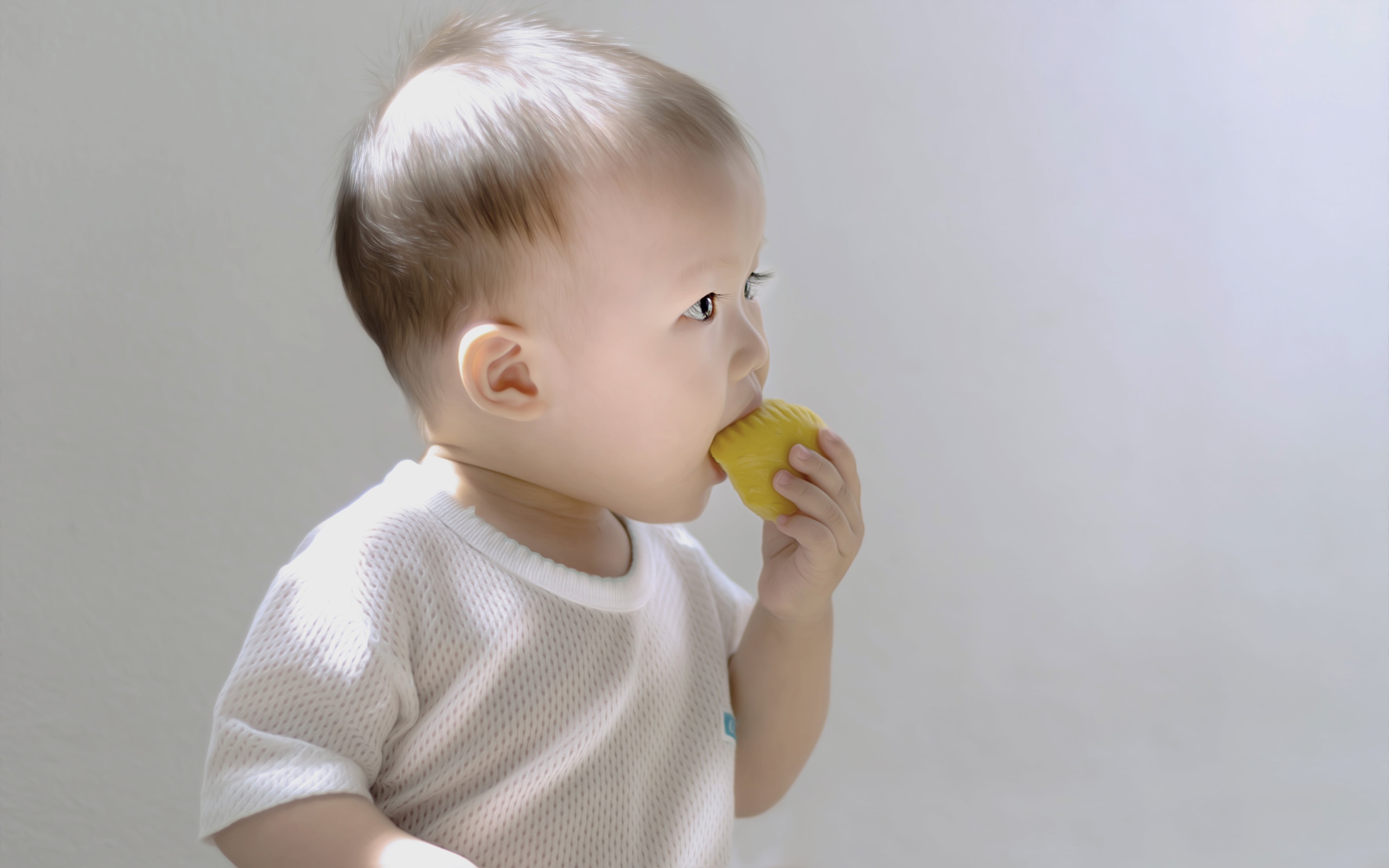 Маленький ребенок грызет игрушку на сером фоне