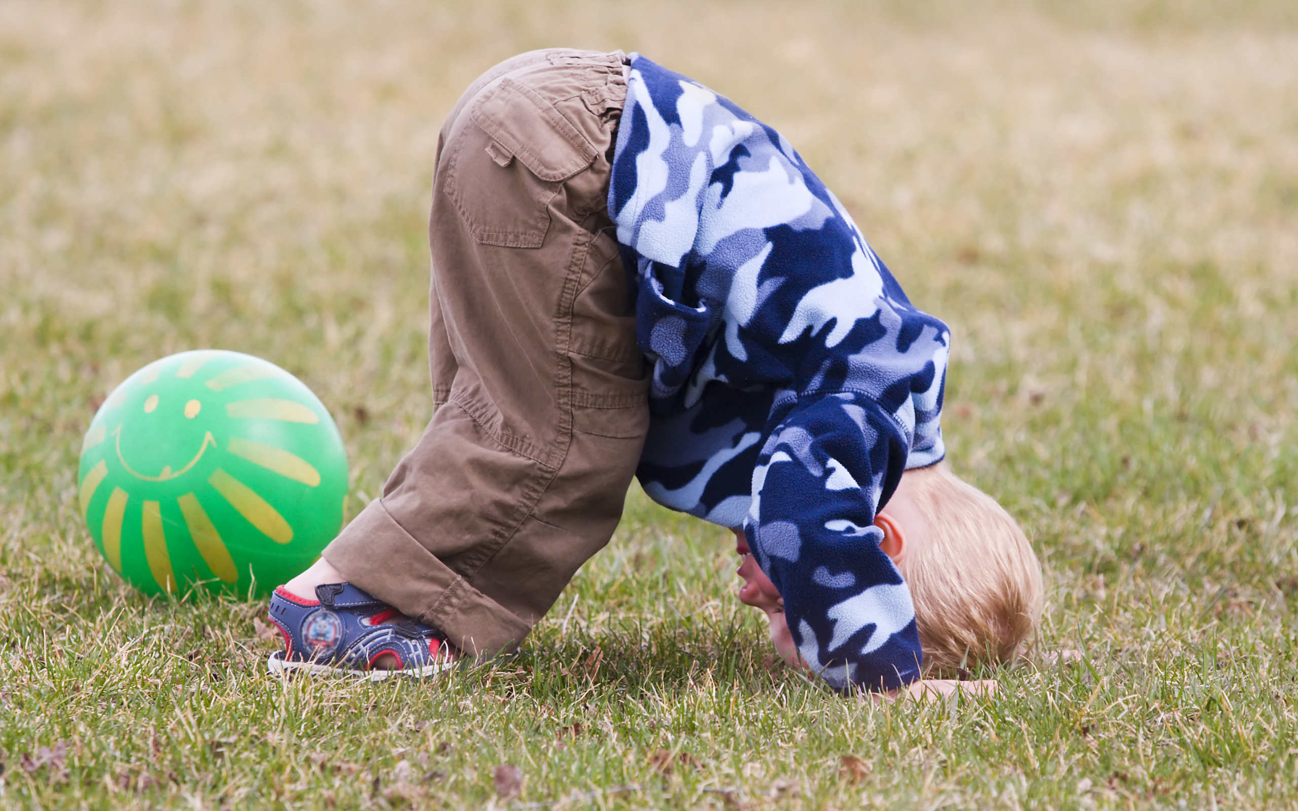 Маленький мальчик играет на траве с мячом
