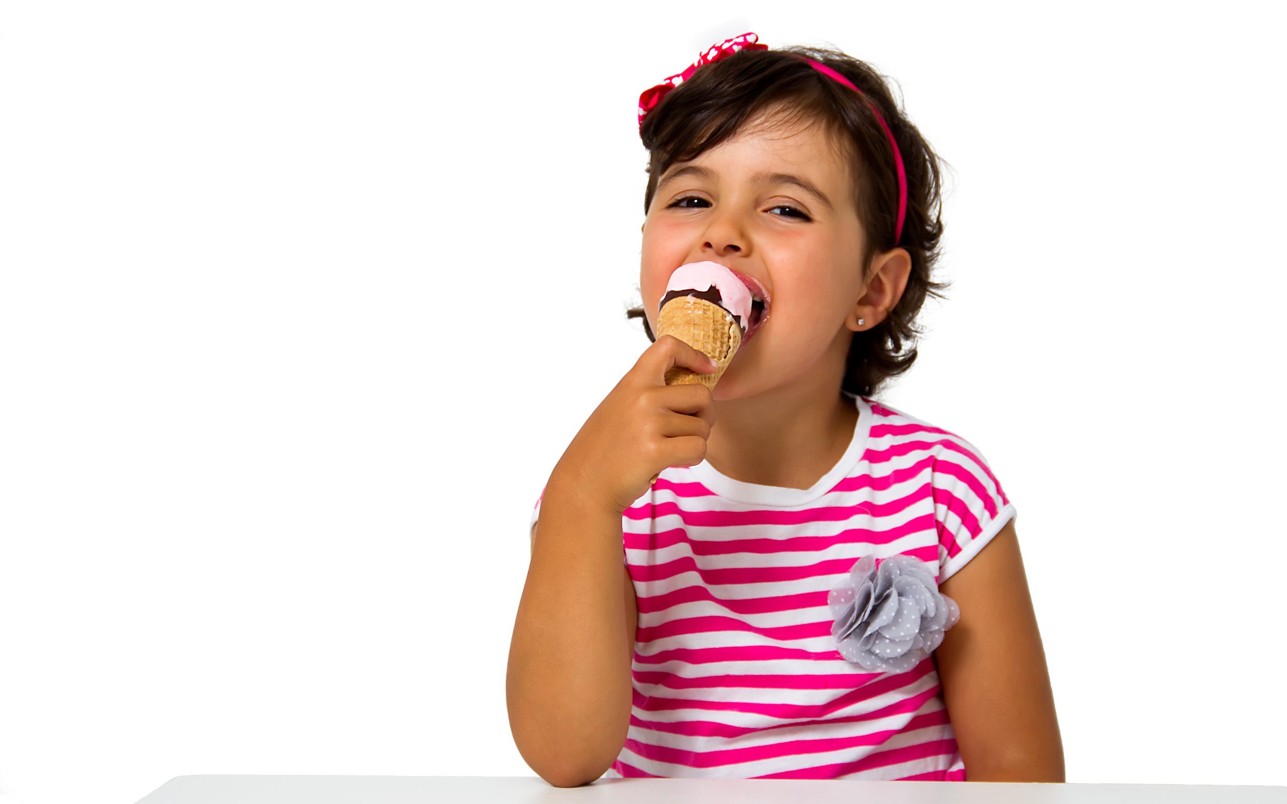 Маленькая девочка ест мороженое за столом на белом фоне