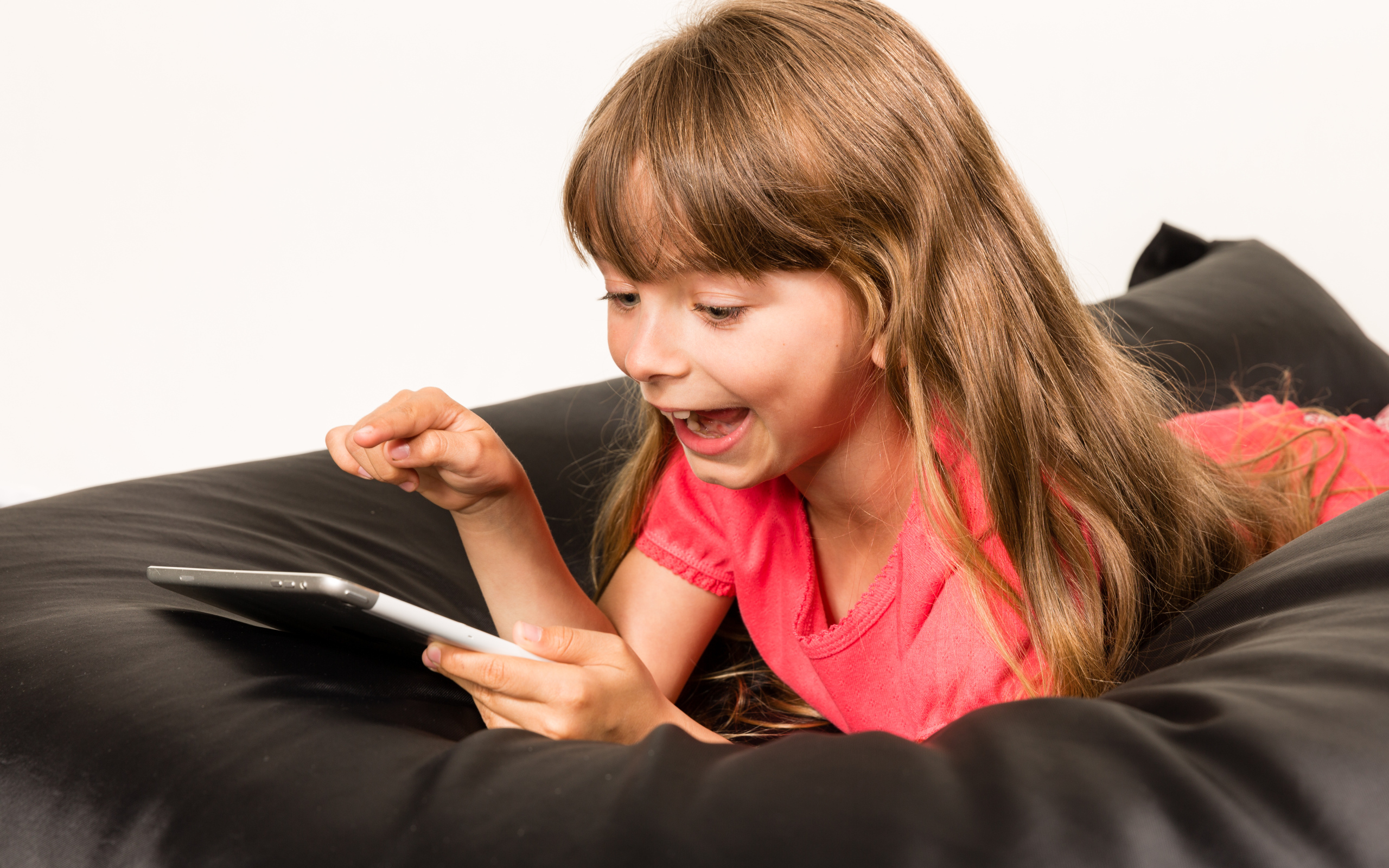 Маленькая улыбающаяся девочка лежит с планшетом