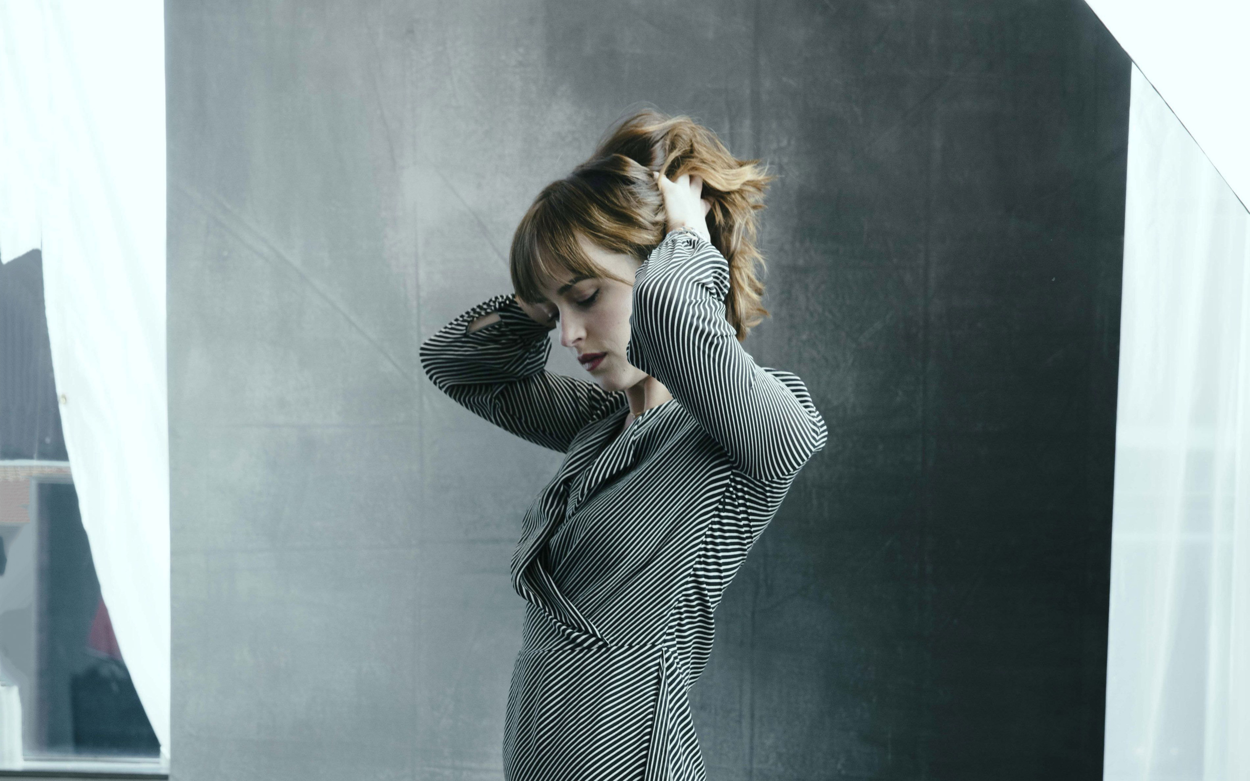 Актриса Дакота Джонсон в платье с руками в волосах