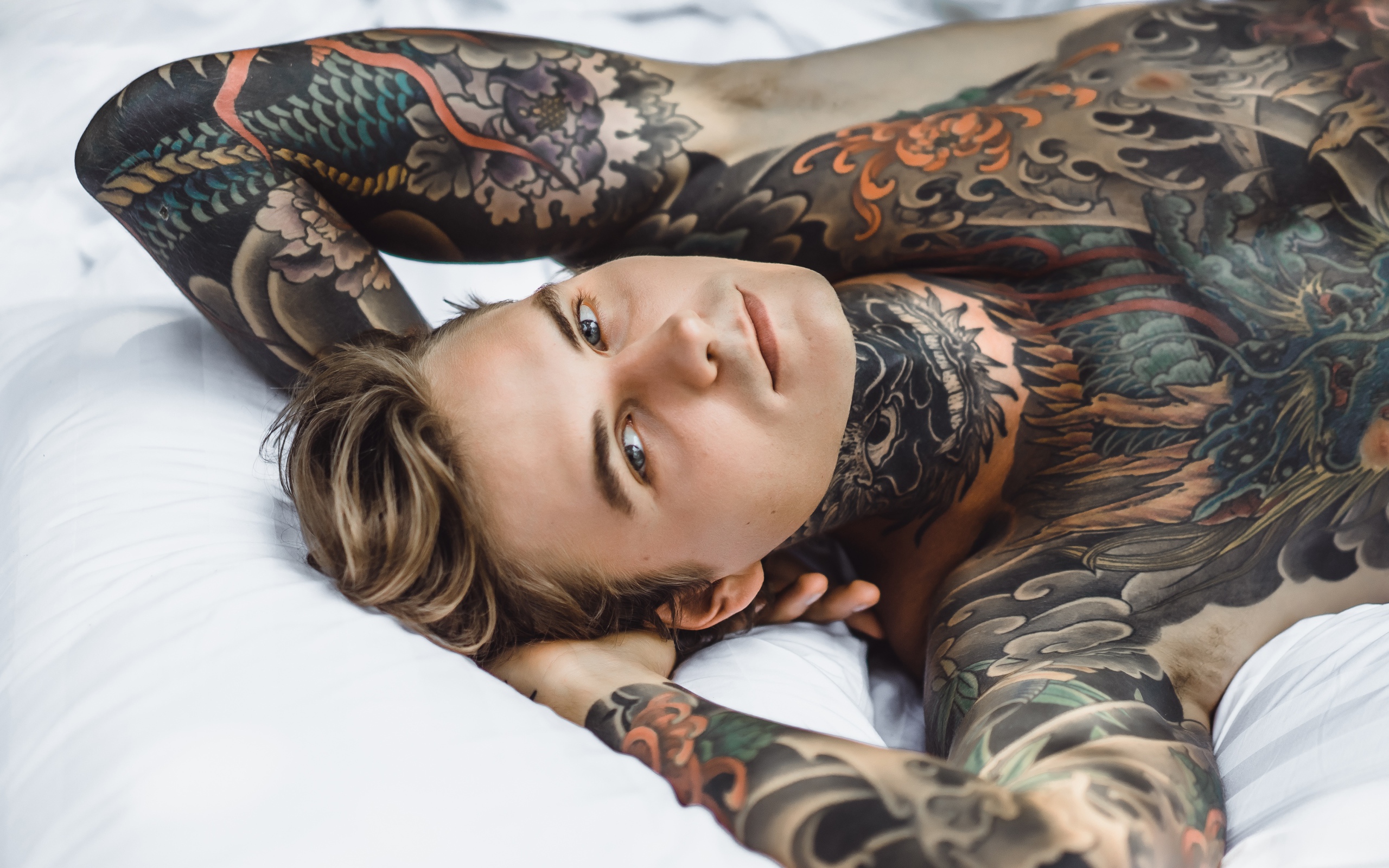 Красивый молодой человек с татуировками на теле лежит на кровати