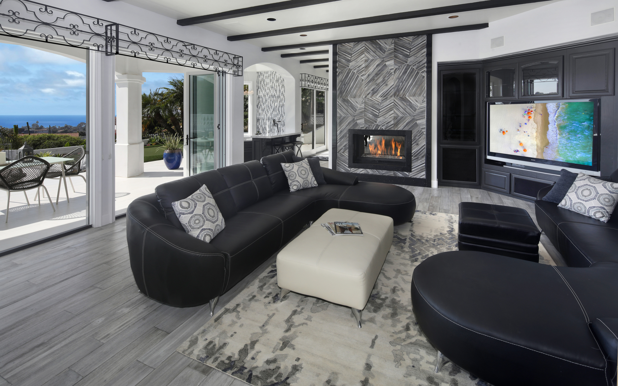 Большая просторная гостиная с черными кожаными диванами, телевизором и камином 