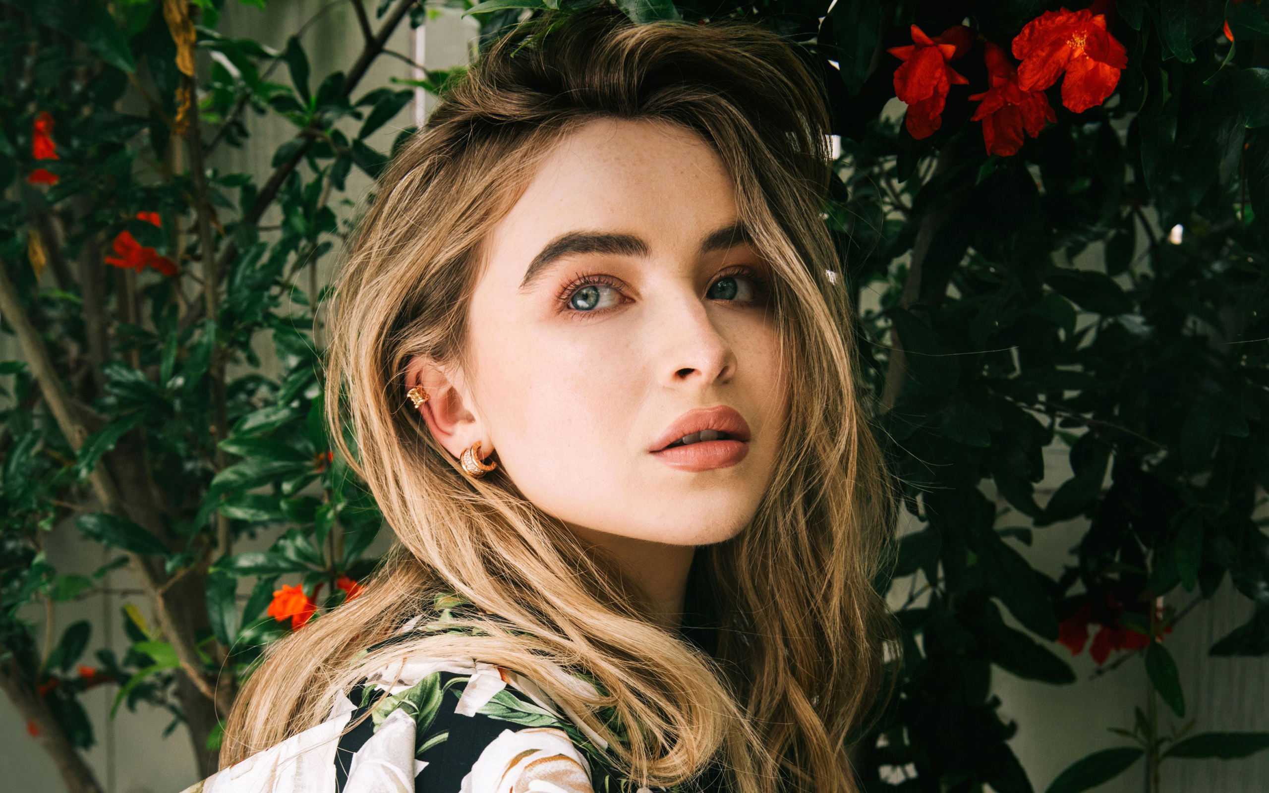 Молодая красивая актриса Сабрина Карпентер у красных цветов