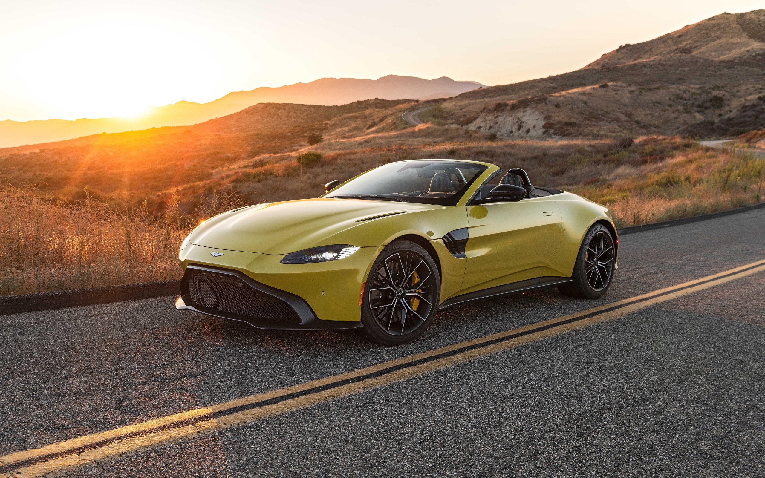 Желтый кабриолет  Aston Martin Vantage Roadster, 2021 года на трассе на рассвете