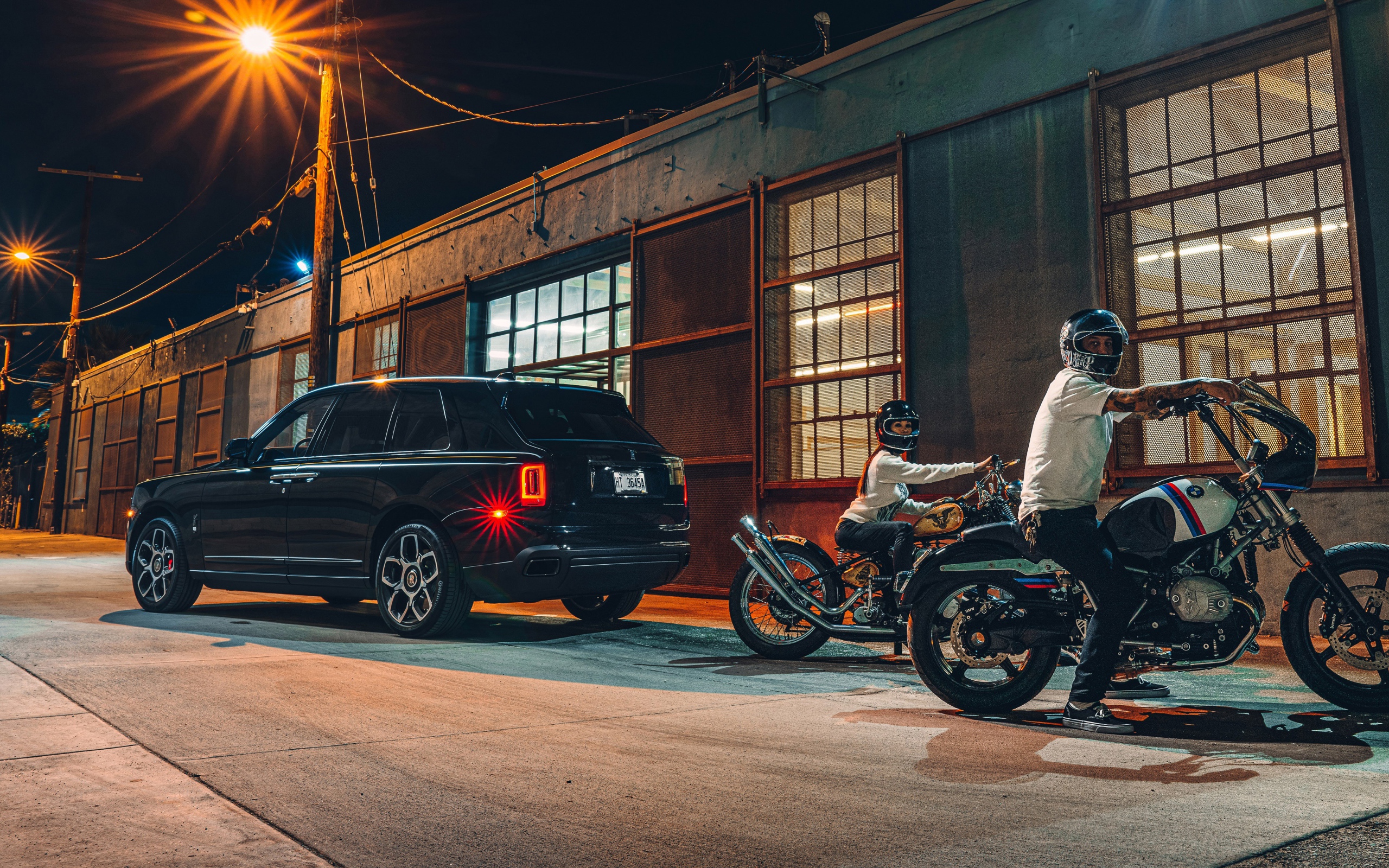 Черный автомобиль Rolls-Royce Cullinan, 2020 года у гаража с байкерами