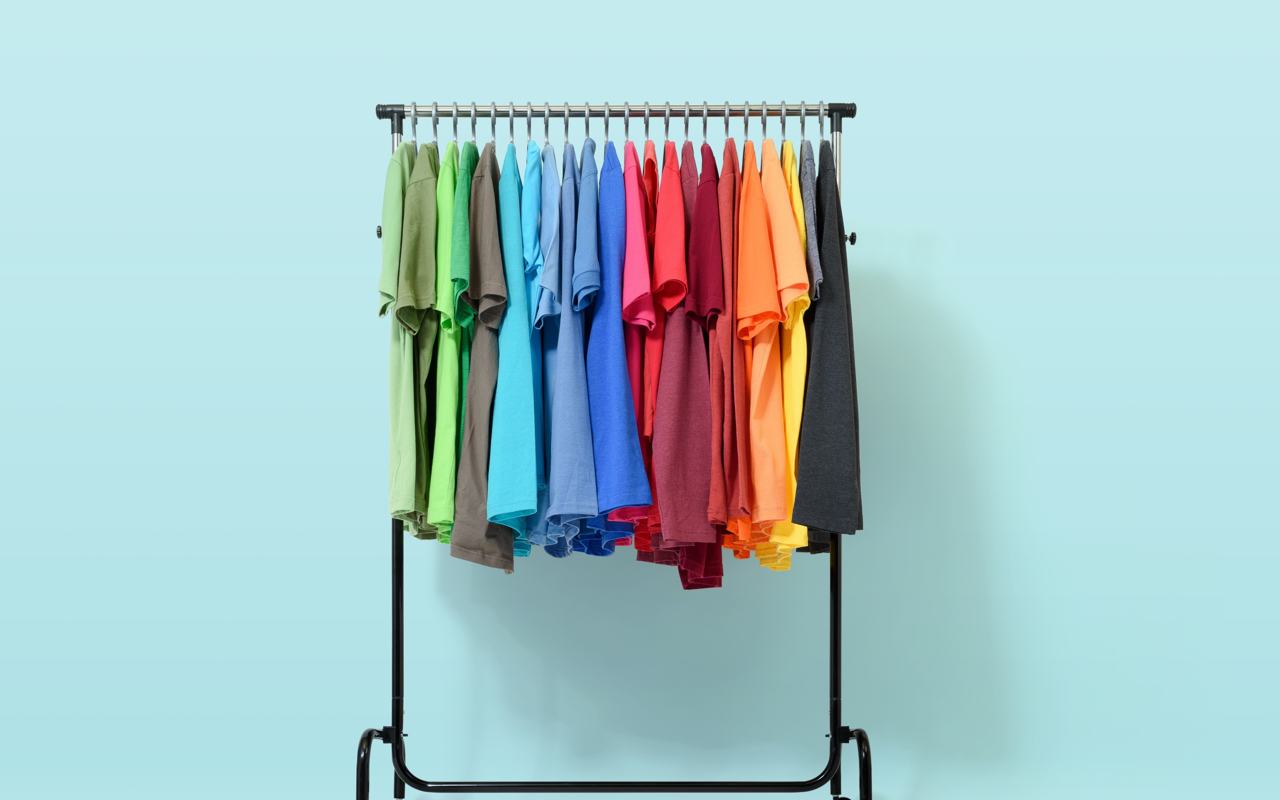 Разноцветные футболки на вешалке на голубом фоне