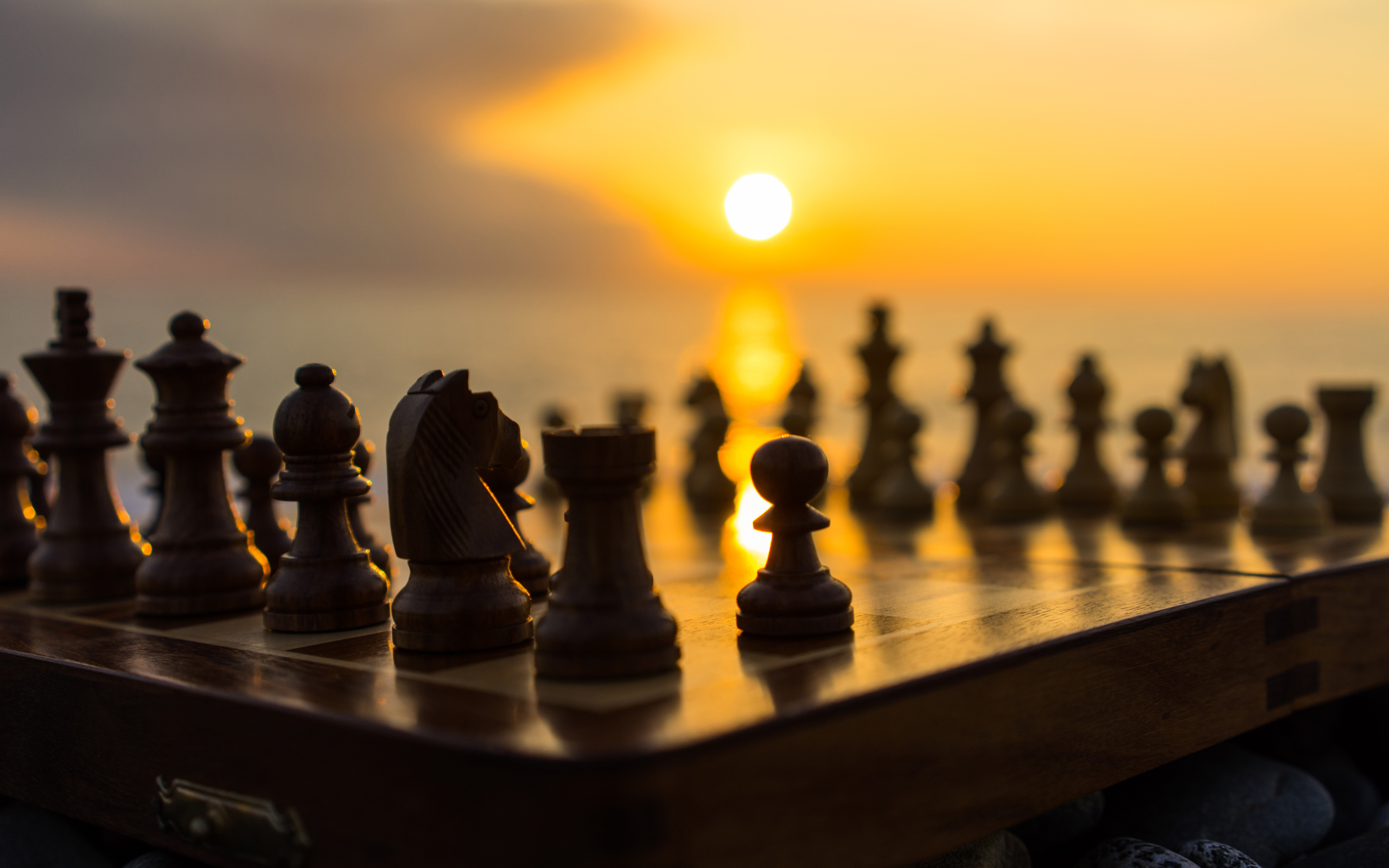 Деревянные шахматы на доске на фоне заката 