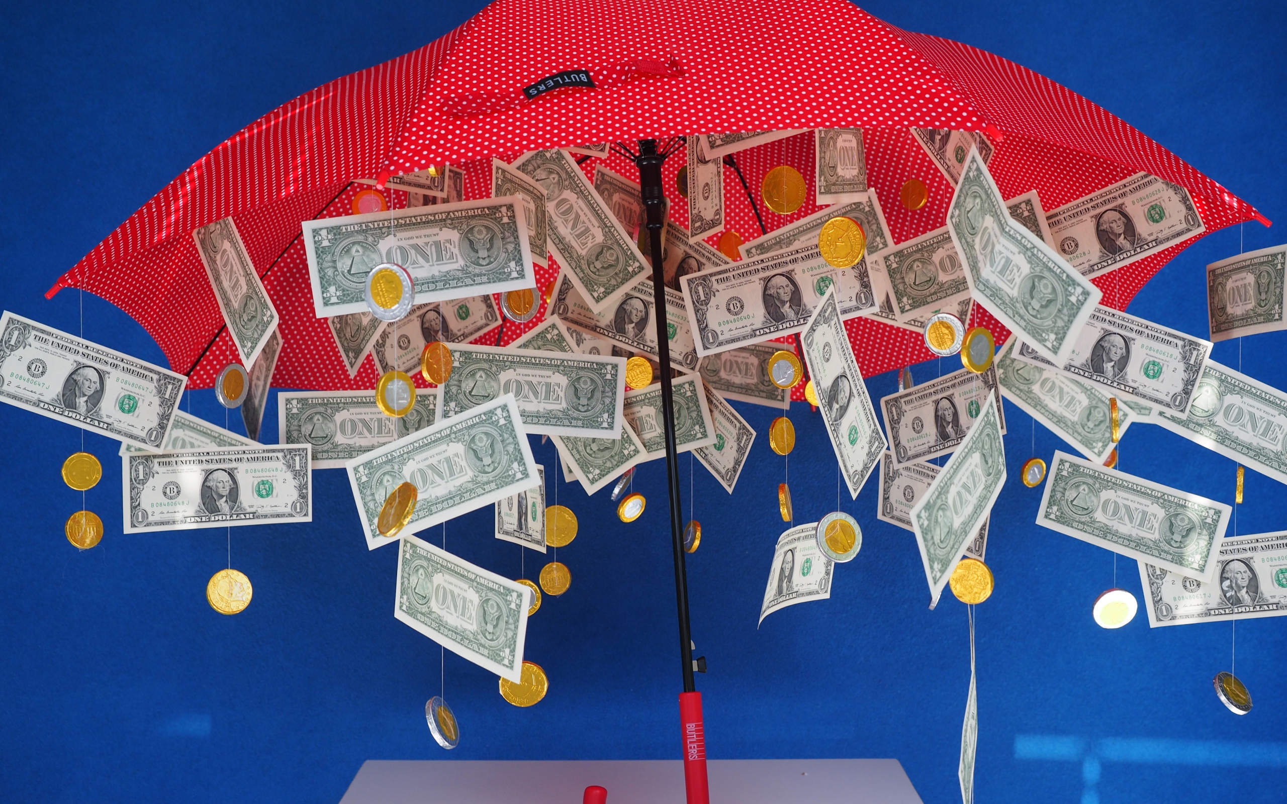 Доллары и монеты высыпаются из зонта на голубом фоне