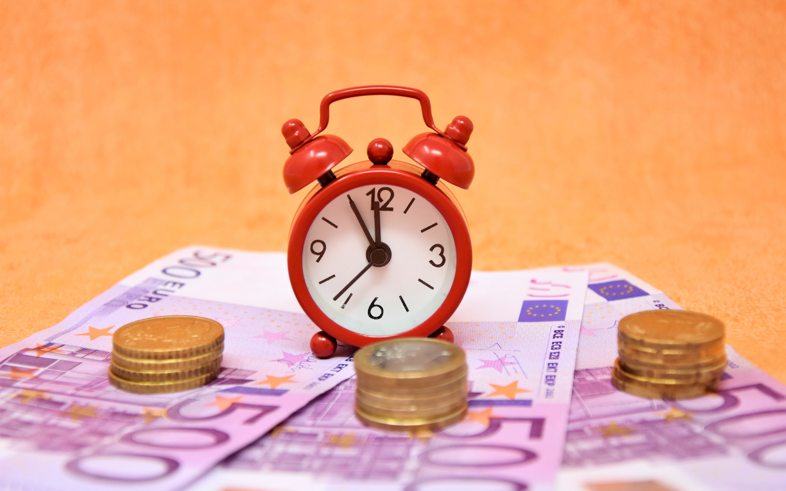 Маленький красный будильник с купюрами евро и монетами