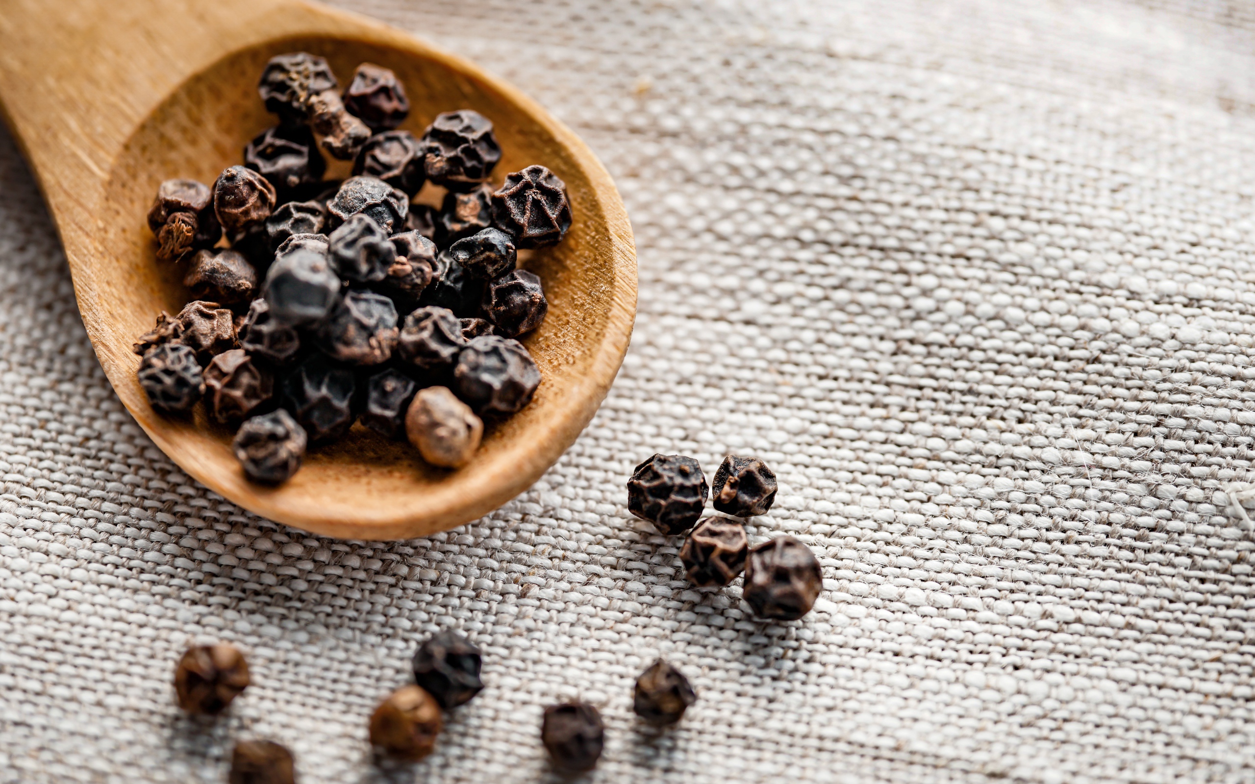 Черный перец горошком на деревянной ложке