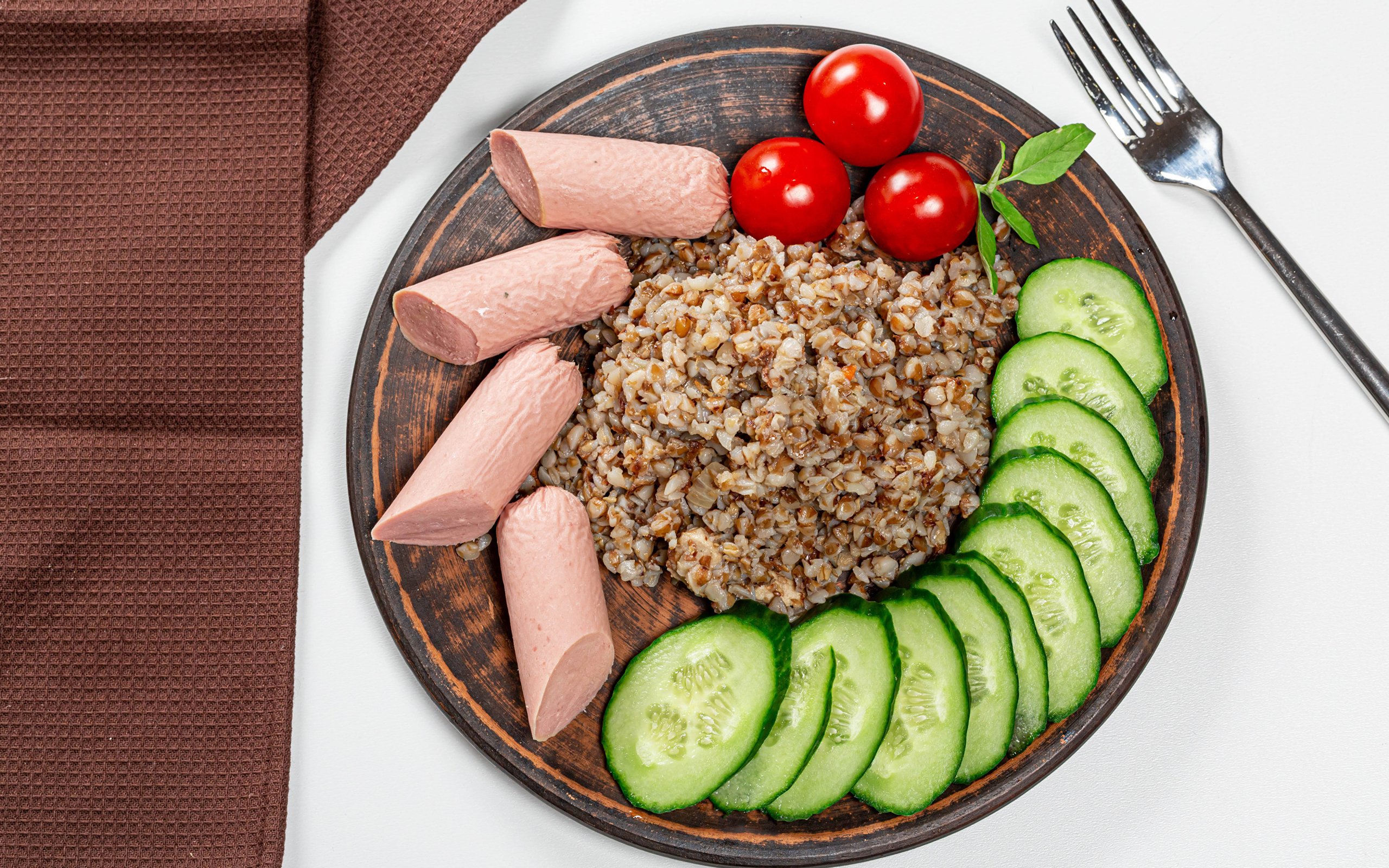 Гречка на тарелке с помидорами, огурцами и сосисками