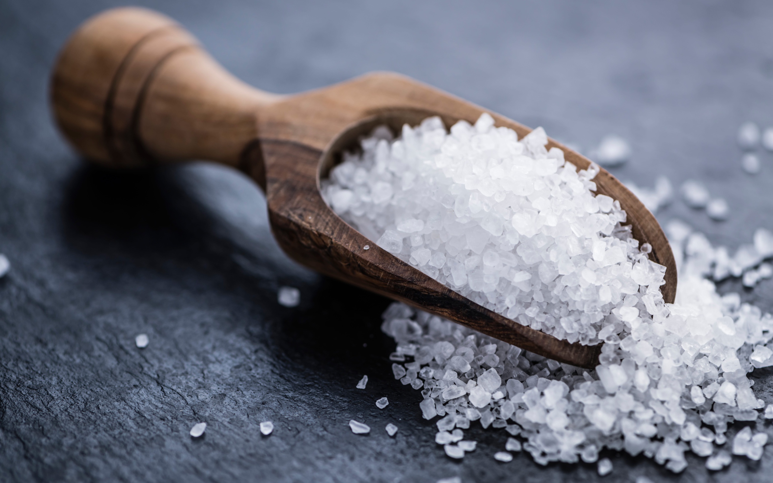Крупная белая соль в лопатке на столе 
