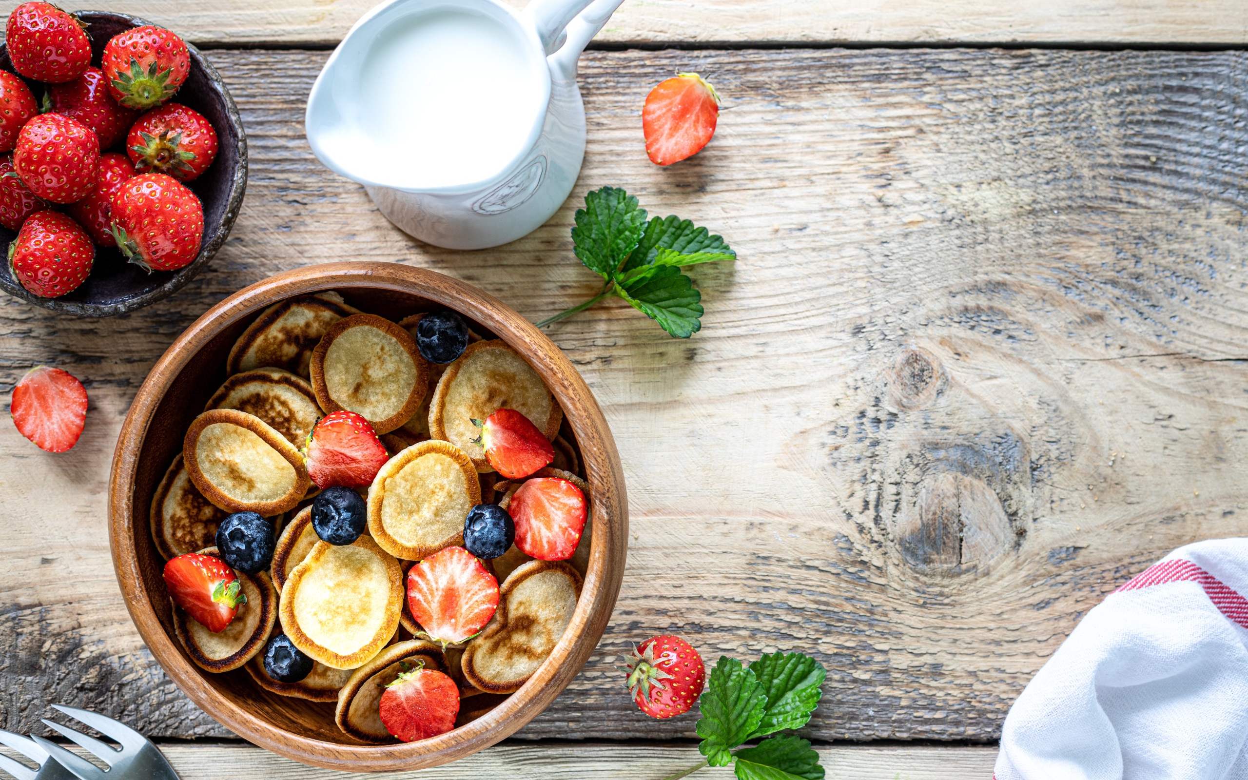 Маленькие оладьи в миске с клубникой и черникой на столе с молоком 