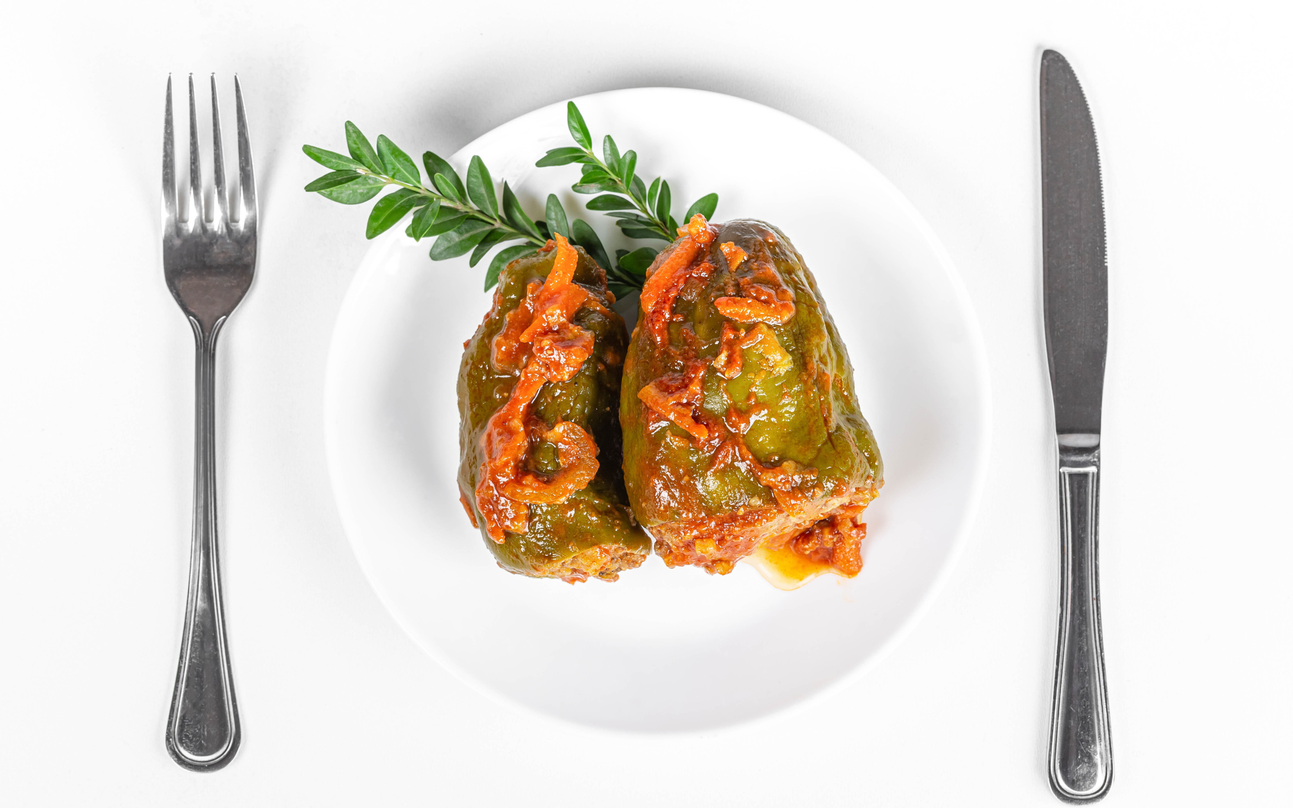 Фаршированный перец на белой тарелке со столовыми приборами