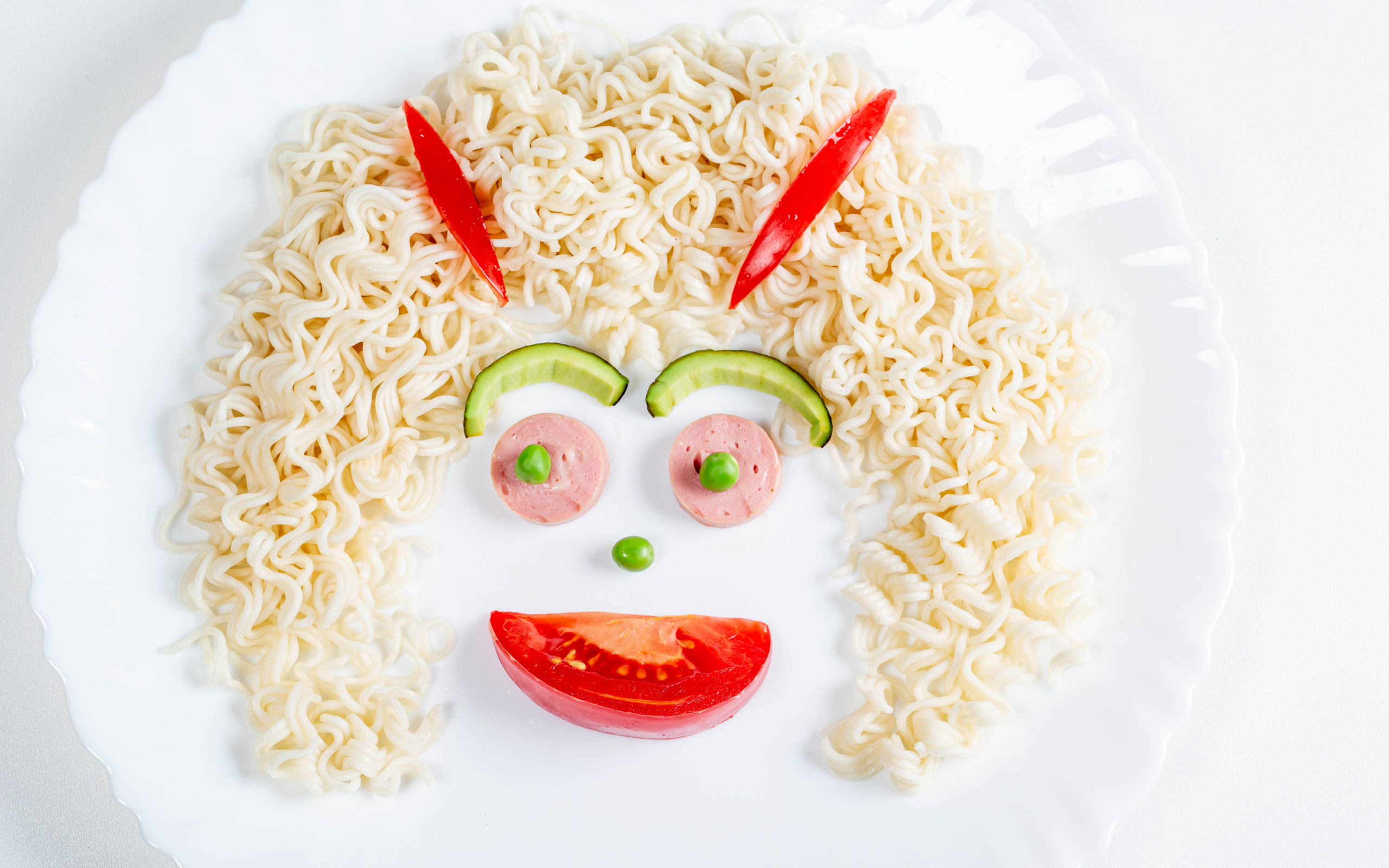 Лицо из вермишели с овощами и колбасой на белой тарелке 