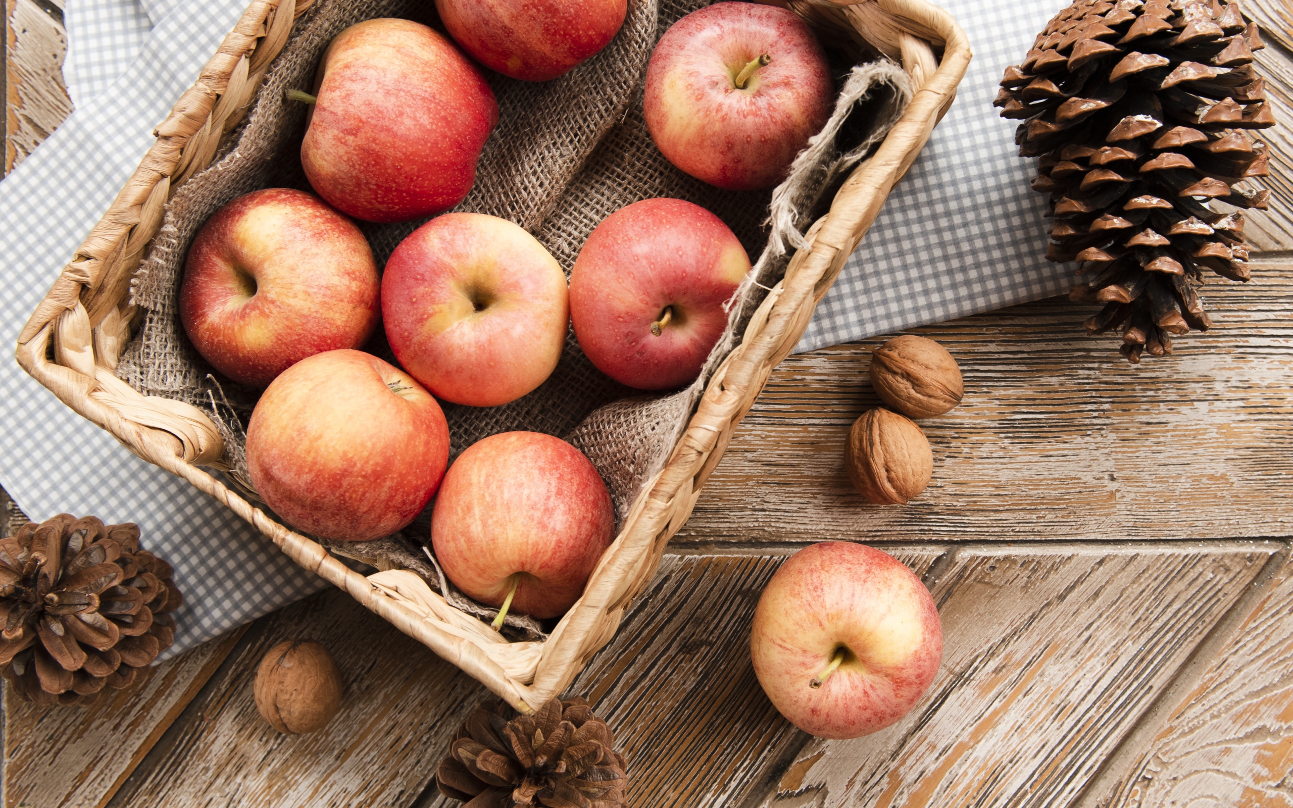 Корзина с яблоками на столе с сосновыми шишками