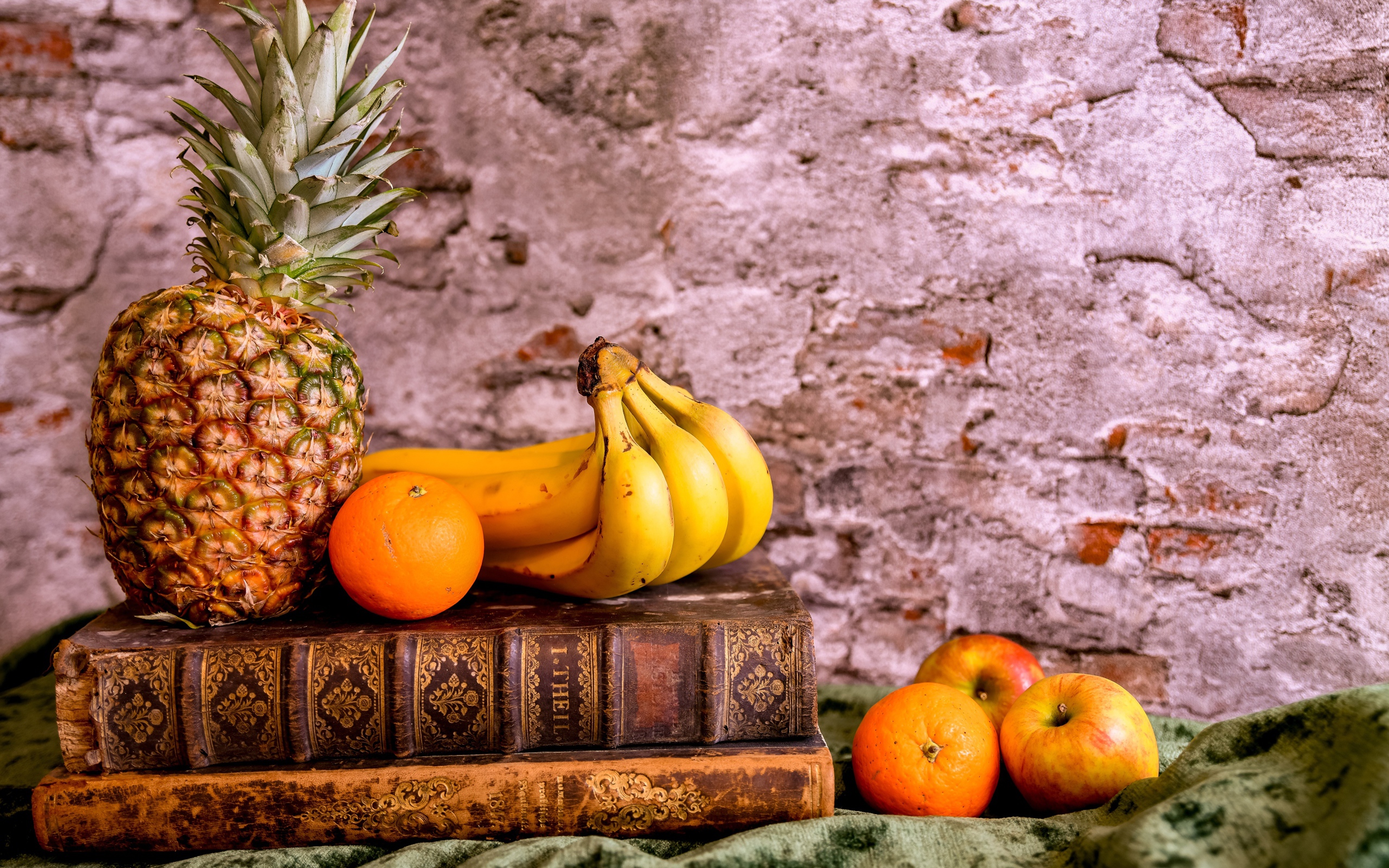 Апельсины, бананы, яблоки и ананас на столе со старыми книгами