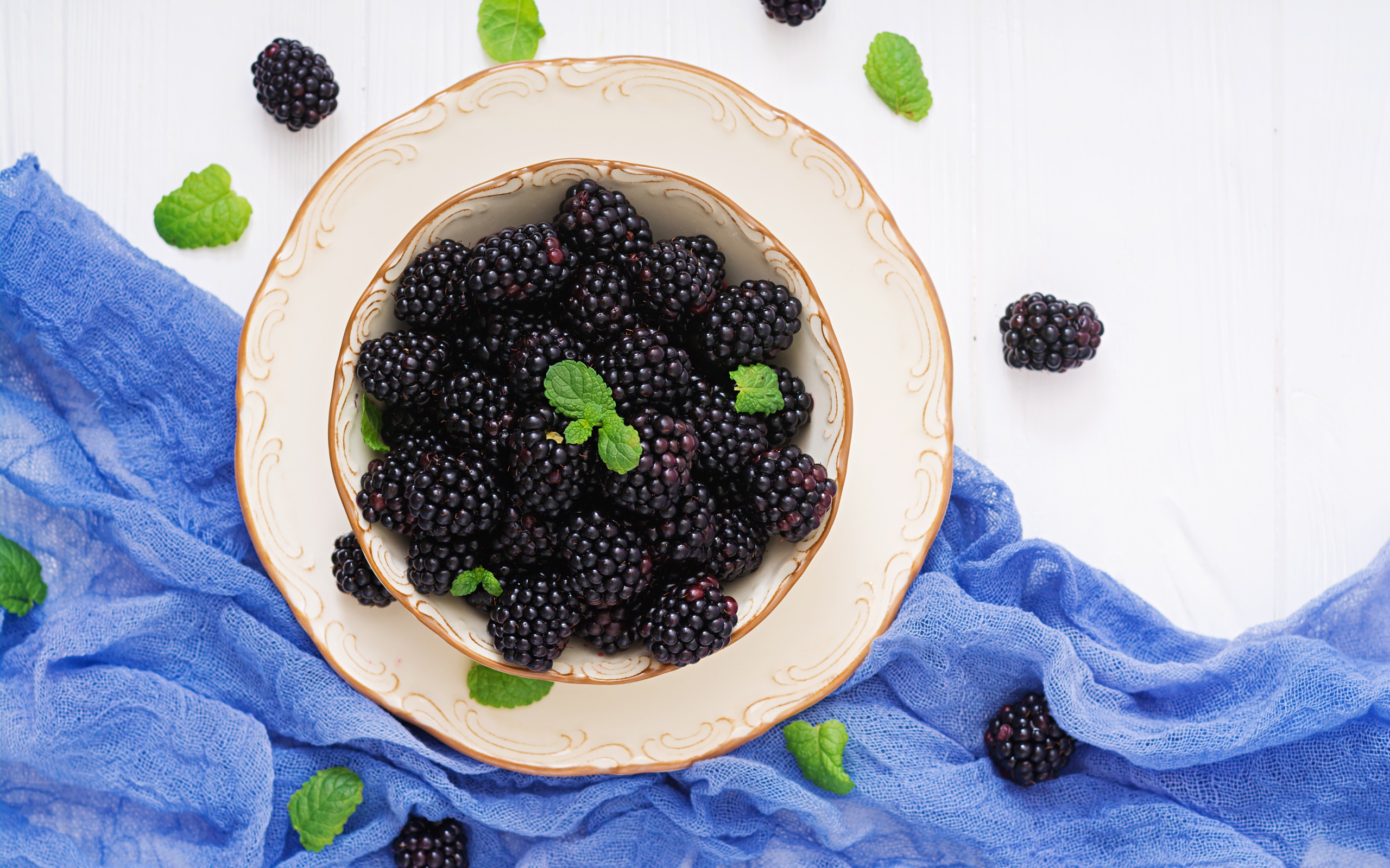 Вкусная спелая ежевика в тарелке на белом фоне с синей тканью 