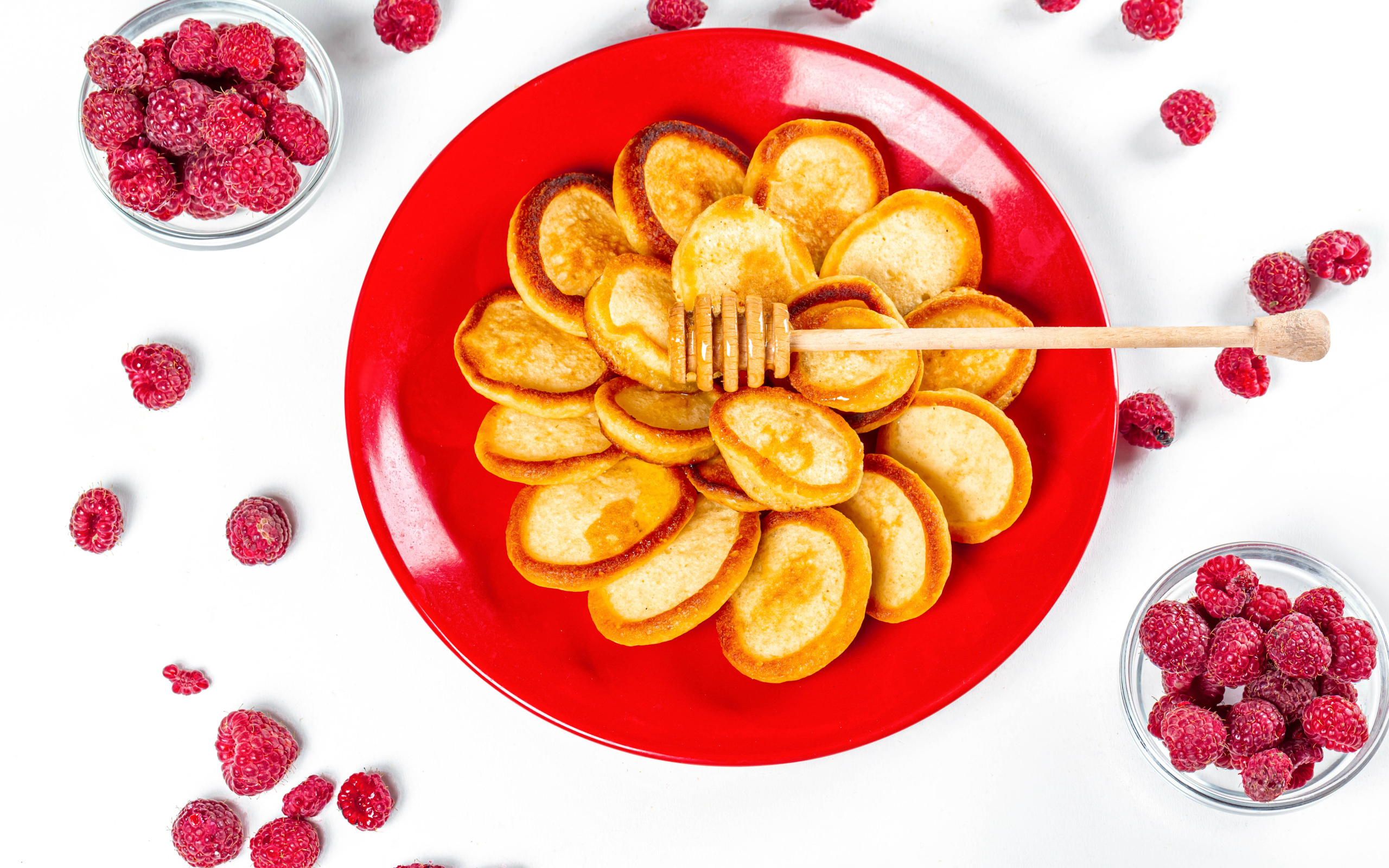 Оладьи на красной с медом на красной тарелке на столе с ягодами малины