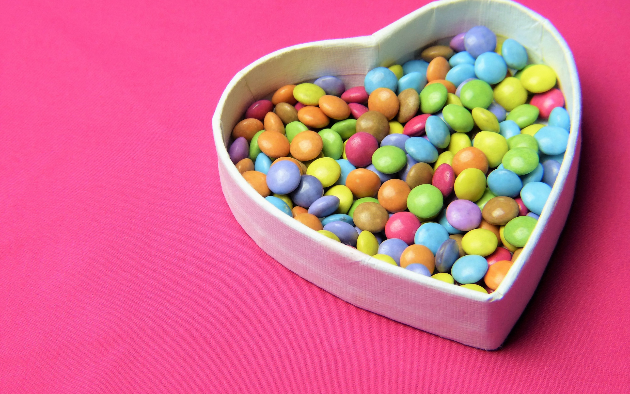 Коробка в форме сердца с разноцветными конфетами на розовом фоне