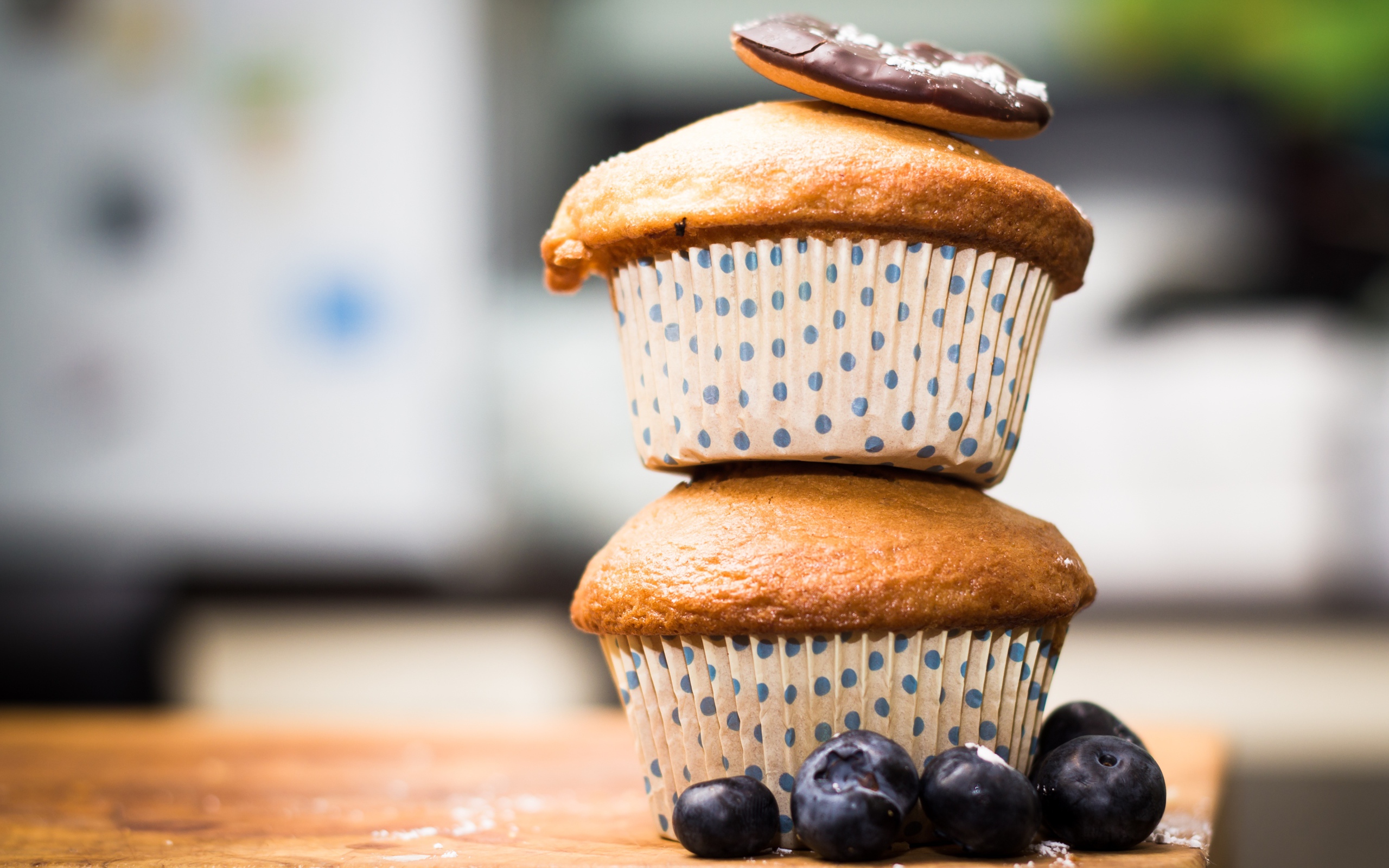 Два кекса стоят на столе с ягодами черники 