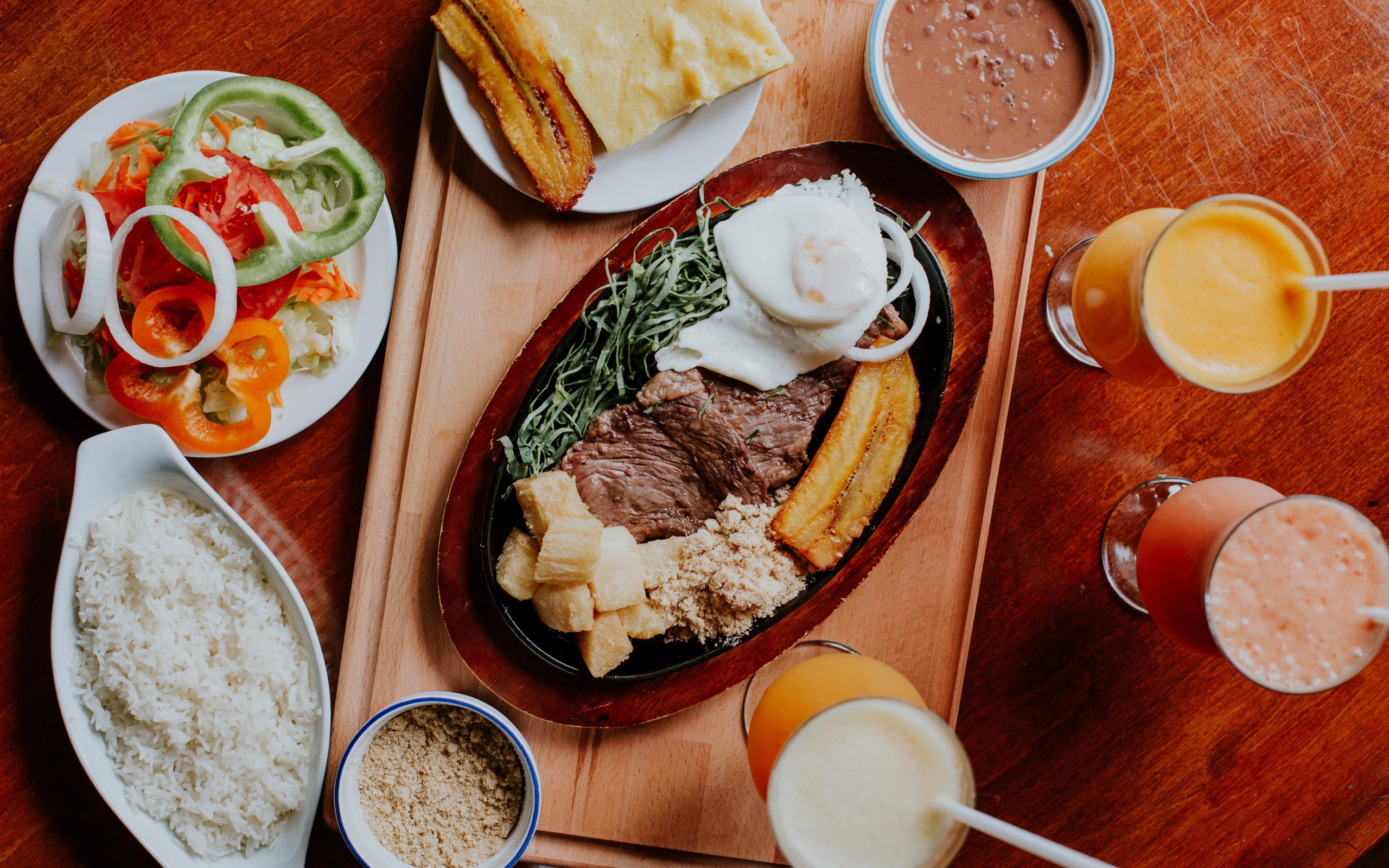 Кусок мяса в жаровне на столе с напитками, овощами и рисом