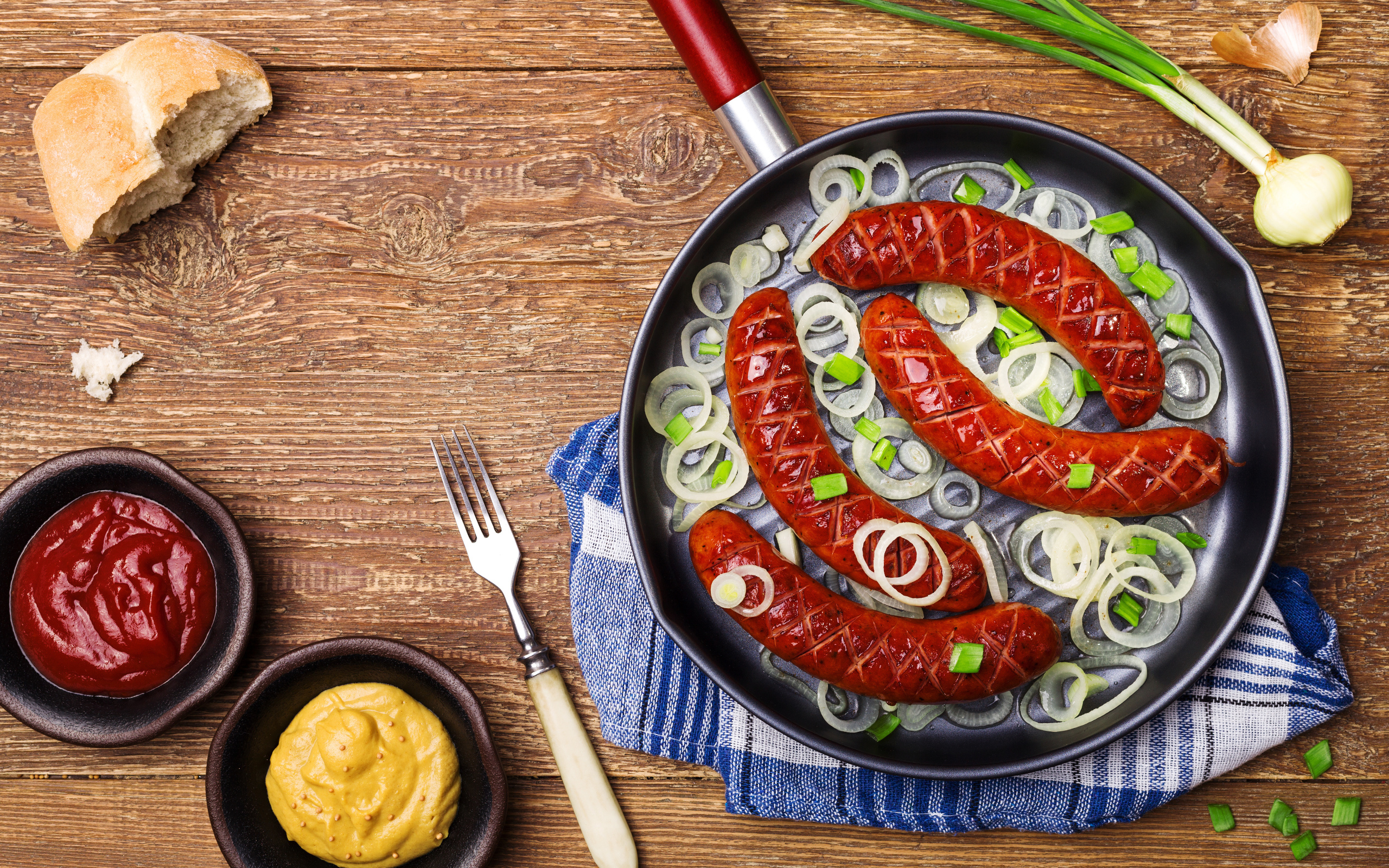 Колбаски барбекю с луком на сковороде на столе с соусом