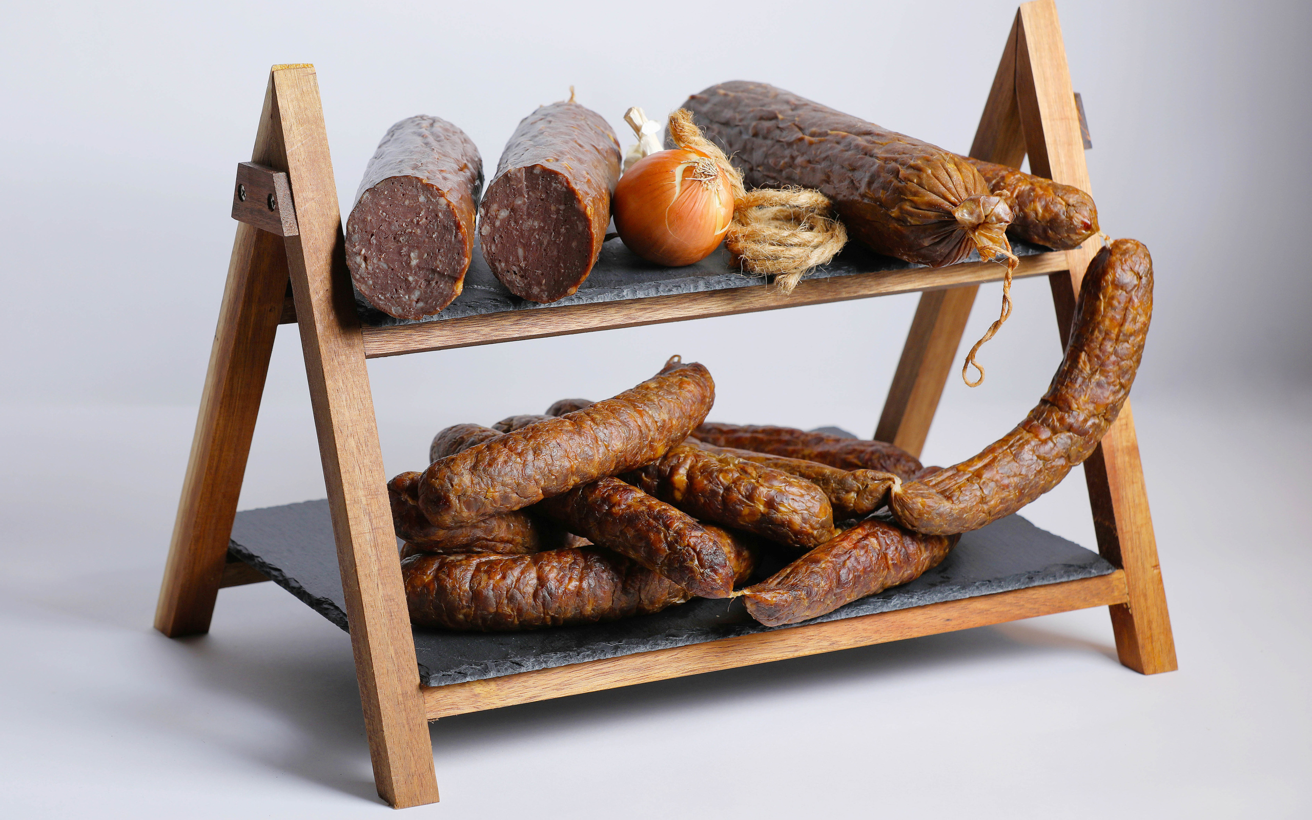 Различные виды колбасы на полке с луком на сером фоне
