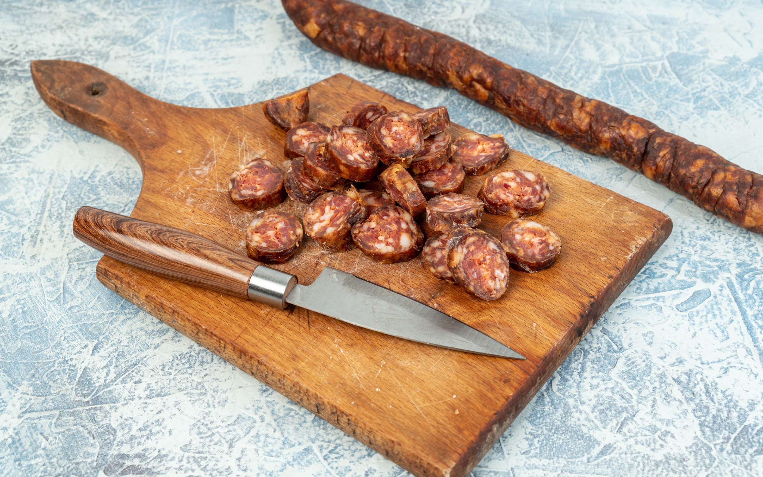 Колбаса нарезана колечками на разделочной доске с ножом 