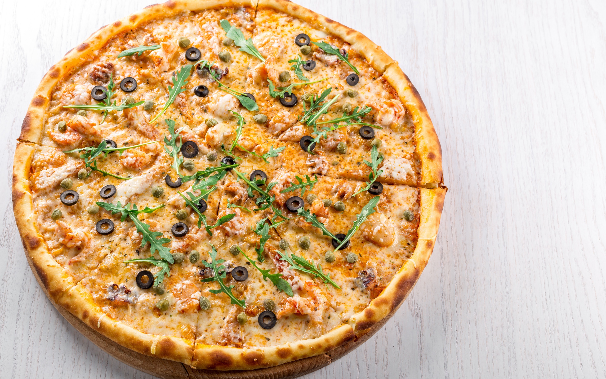 Пицца с морепродуктами, рукколой и оливками на столе 