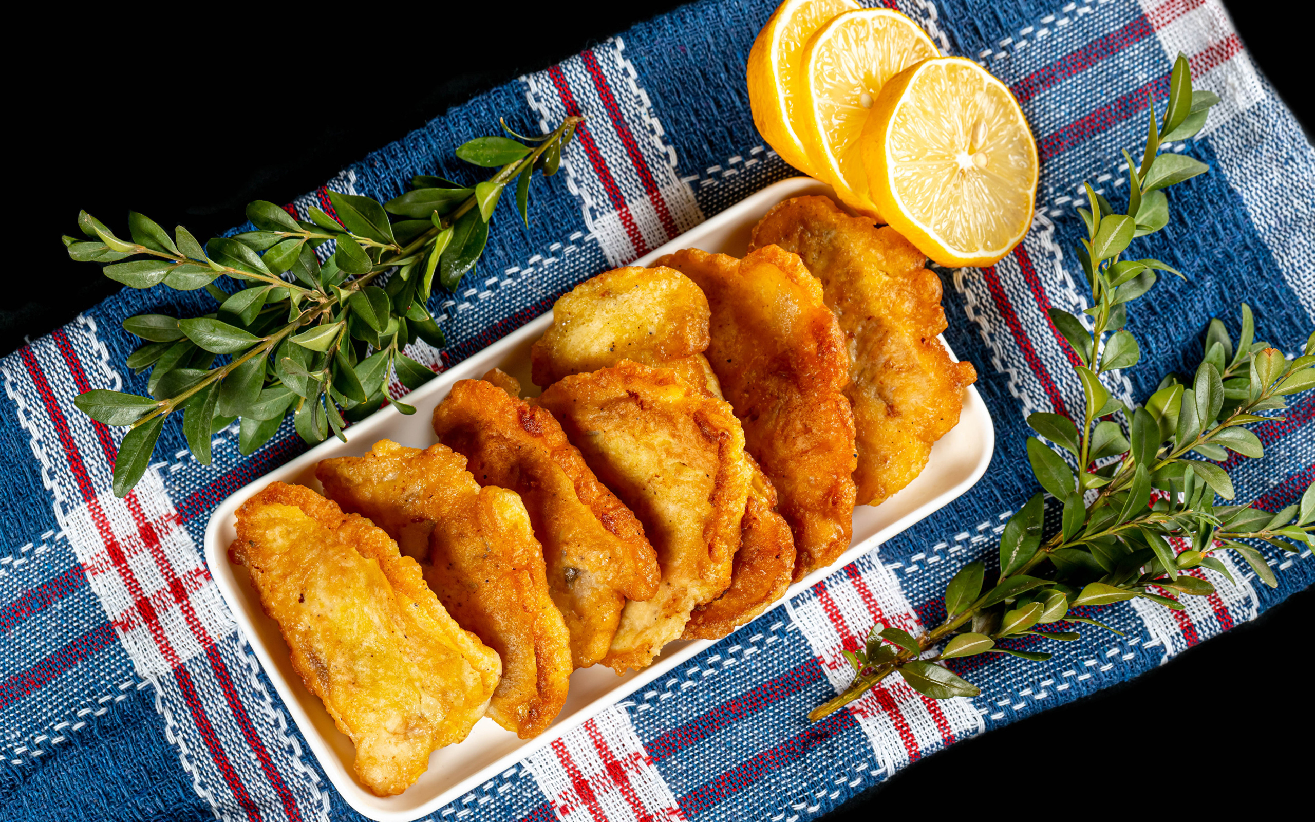 Жареная рыба в кляре на столе с лимоном и зеленью