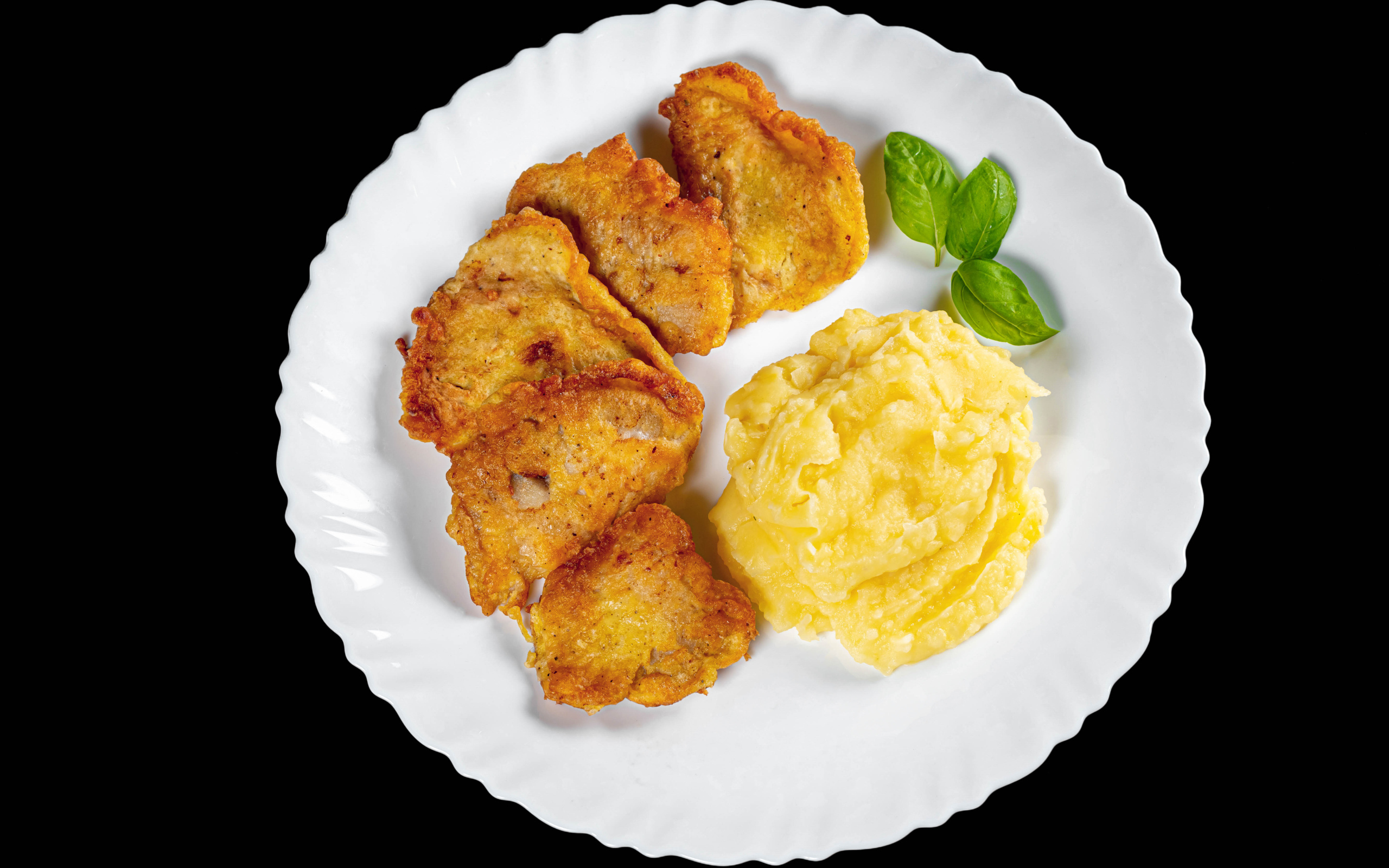 Куски жареной рыбы с картофельным пюре в тарелке на черном фоне