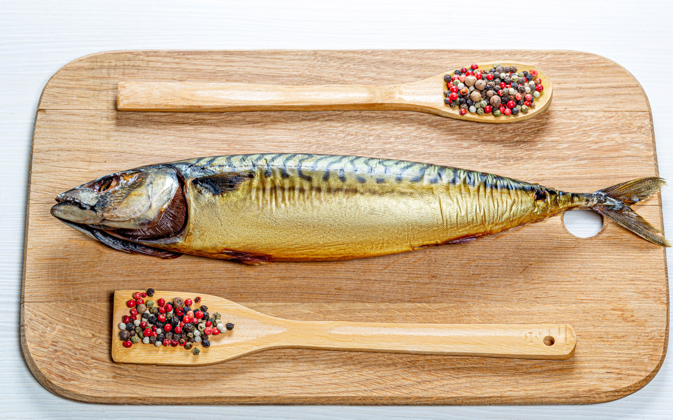 Smoked mackerel on a cutting board with pepper on a white background
