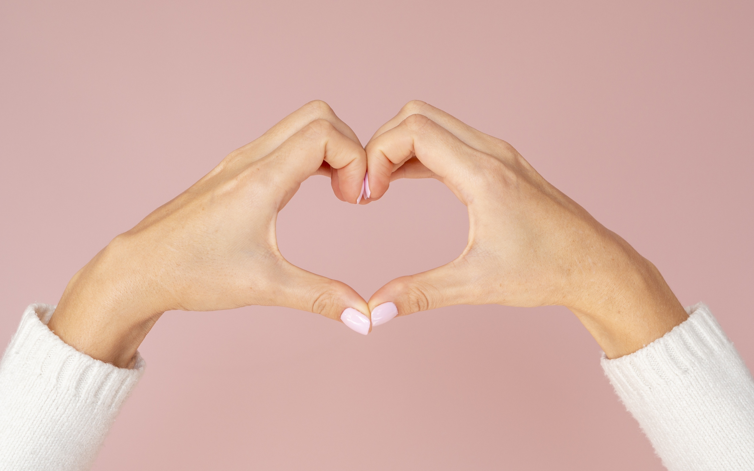 Девушка делает сердце руками на розовом фоне 