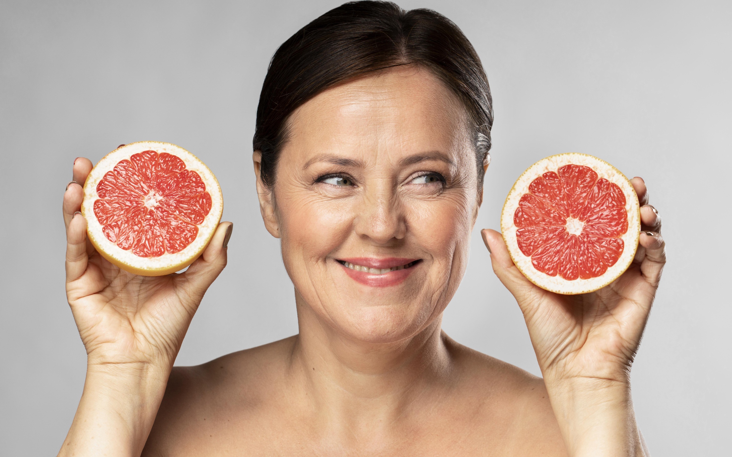 Smiling woman with grapefruit in hands on gray background
