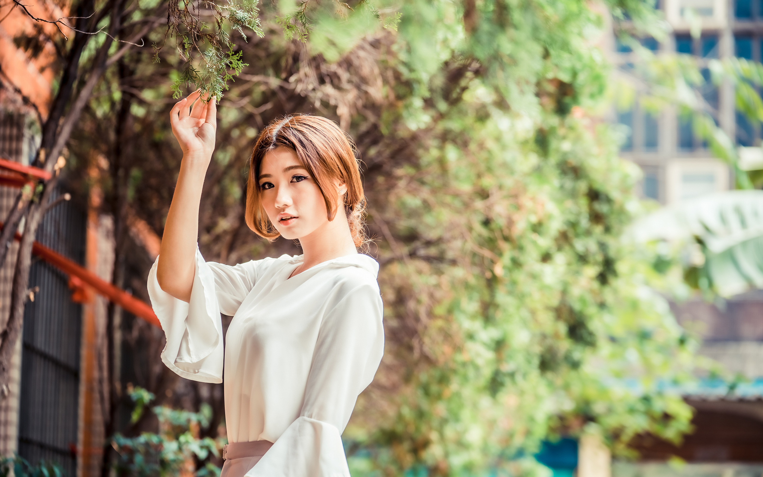 Молодая азиатка в белой блузке стоит у дерева 
