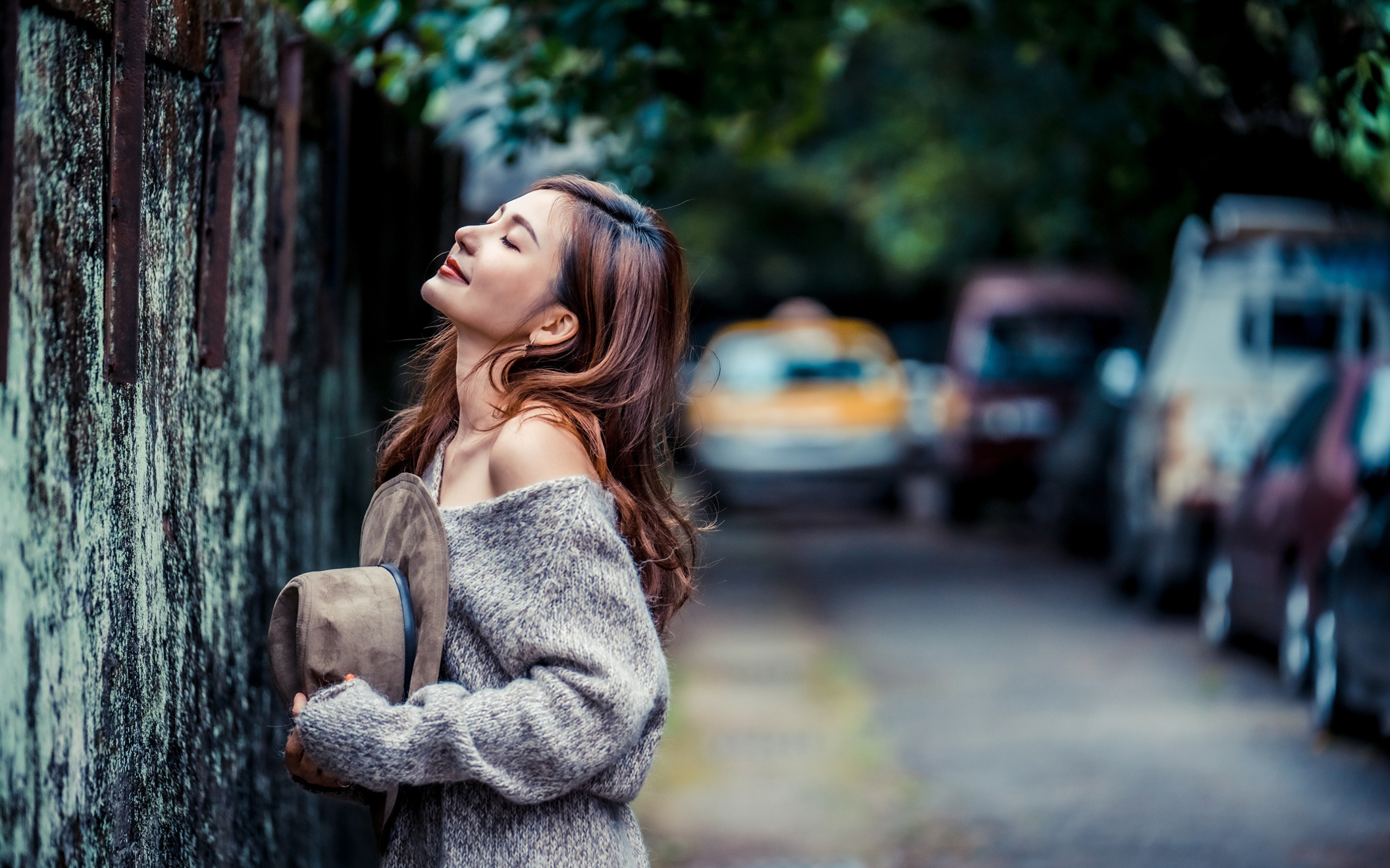 Девушка азиатка в теплом свитере стоит у забора