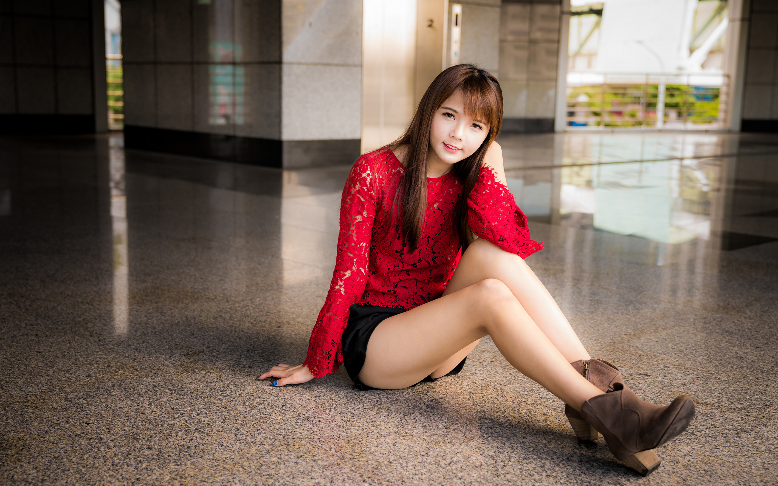 Красивая девушка азиатка в красной блузке сидит на полу