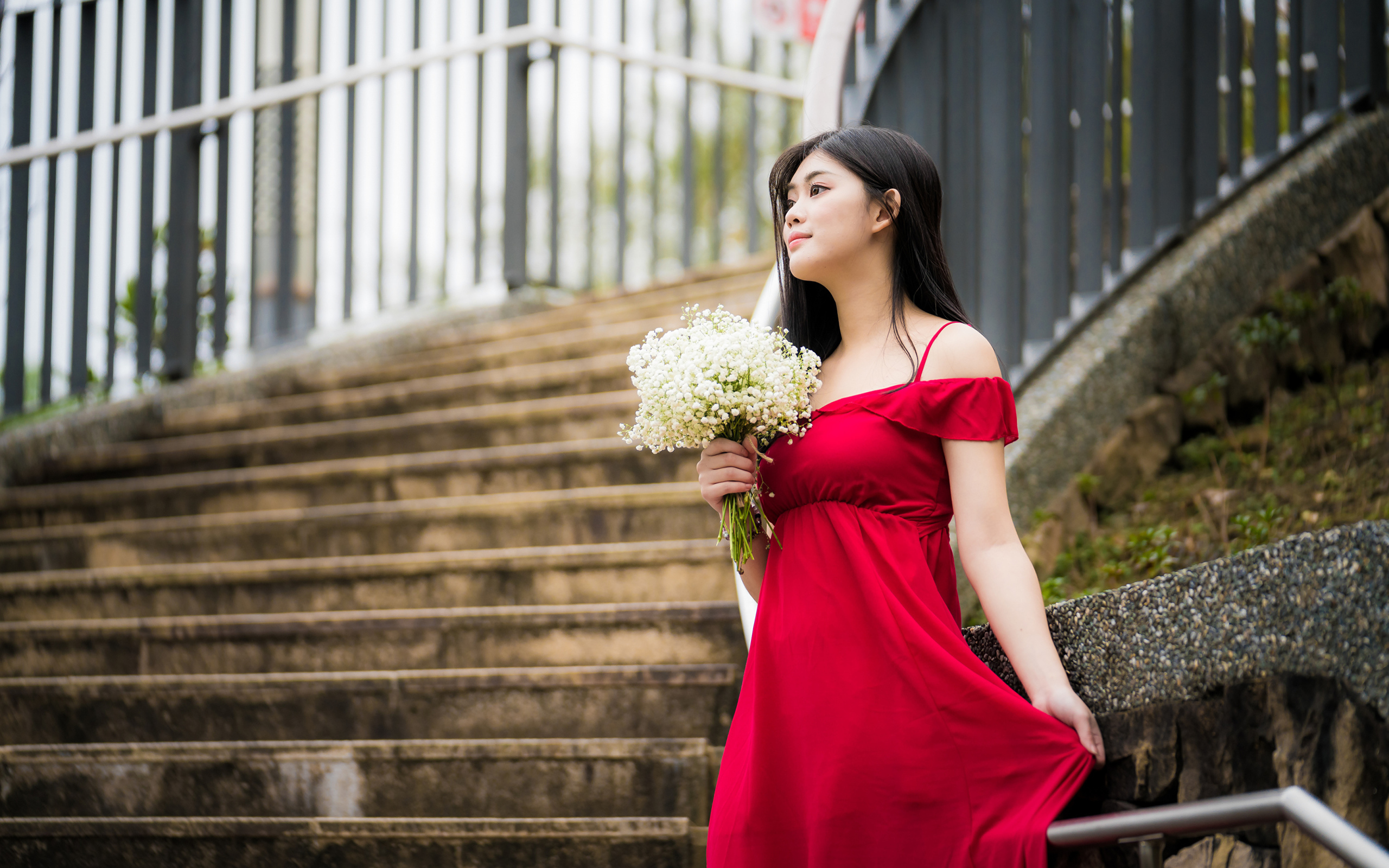 Красивая азиатка в красном платье стоит на ступеньках с букетом ландышей